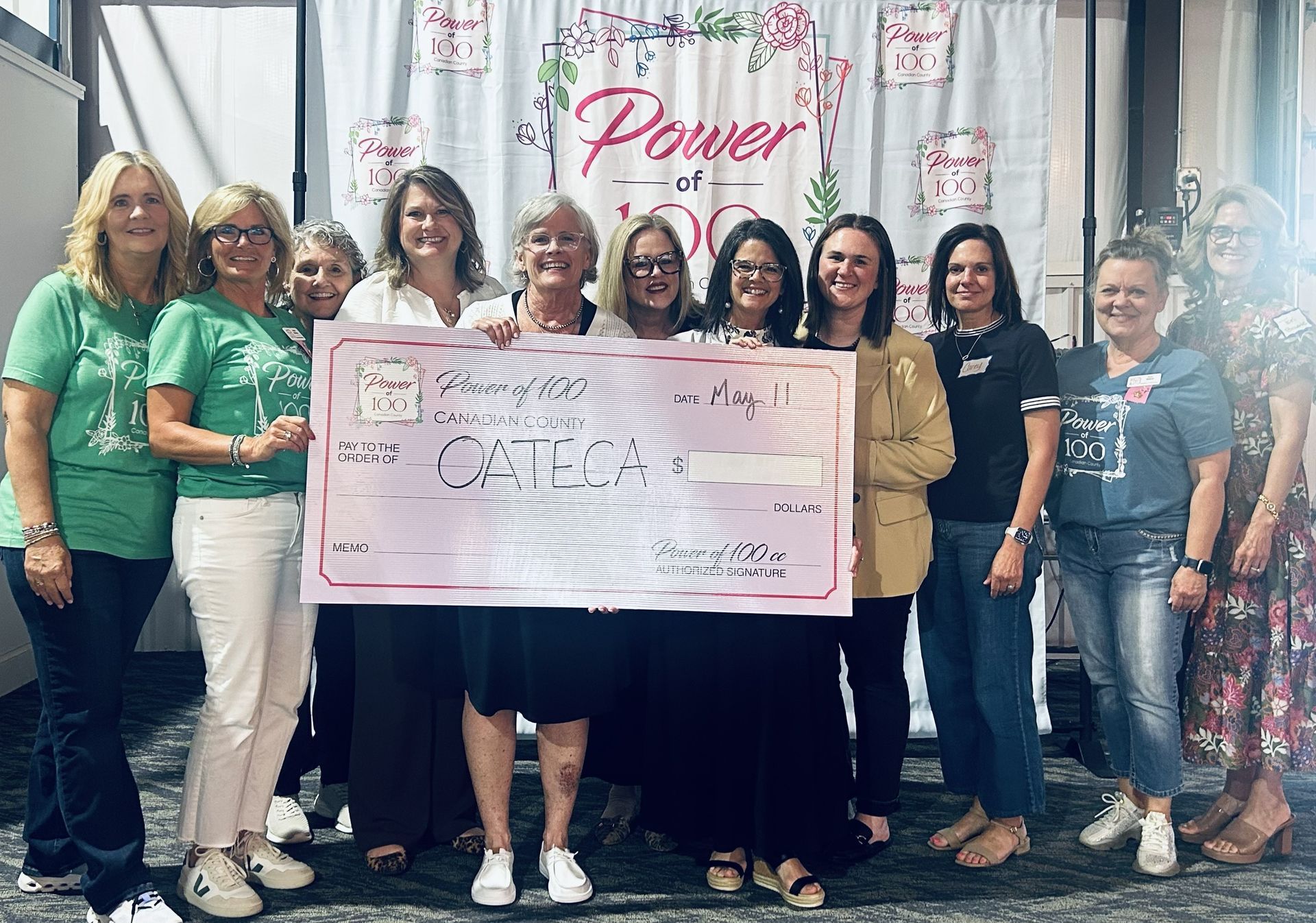 A group of people standing next to each other holding a large pink check.