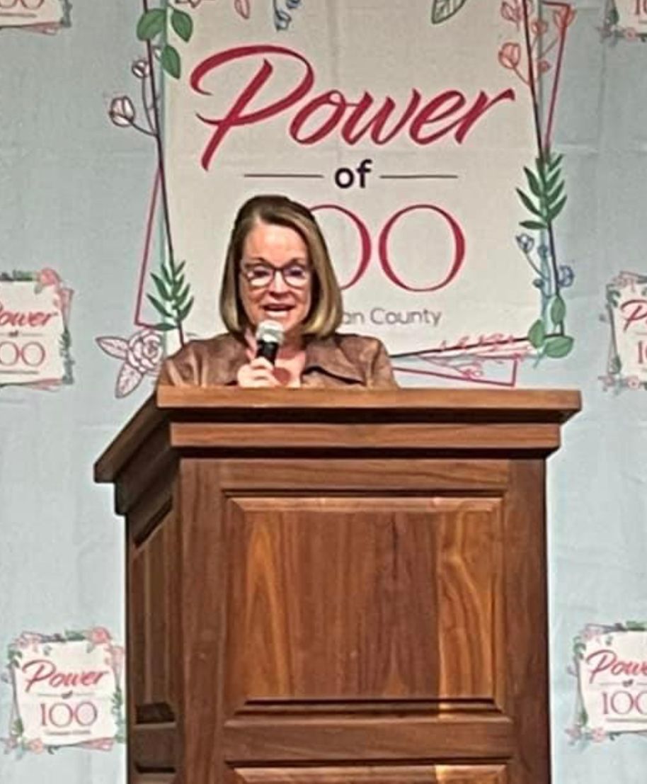 A woman is standing at a podium in front of a sign that says power of do