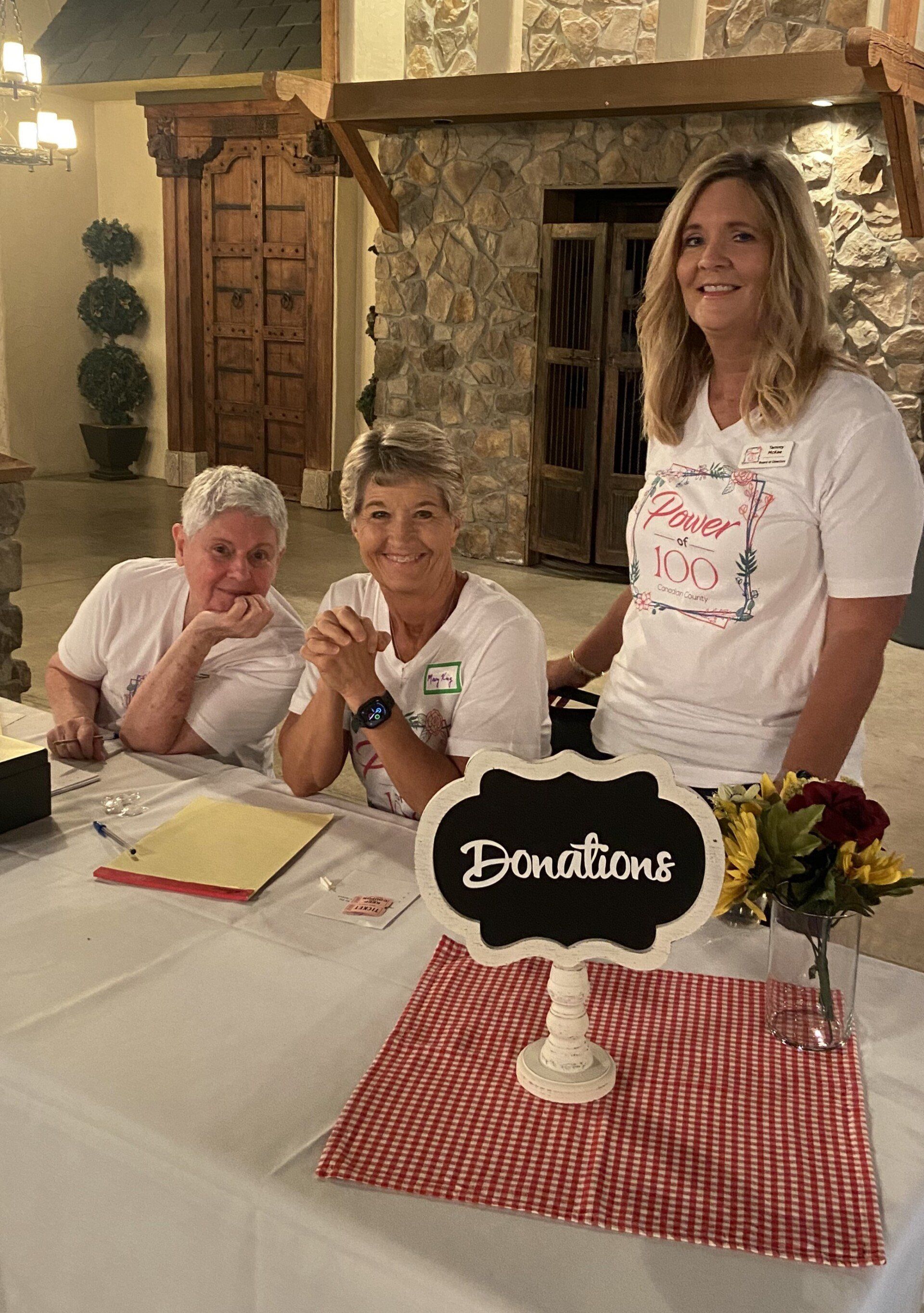 Three women are sitting at a table with a sign that says donations.