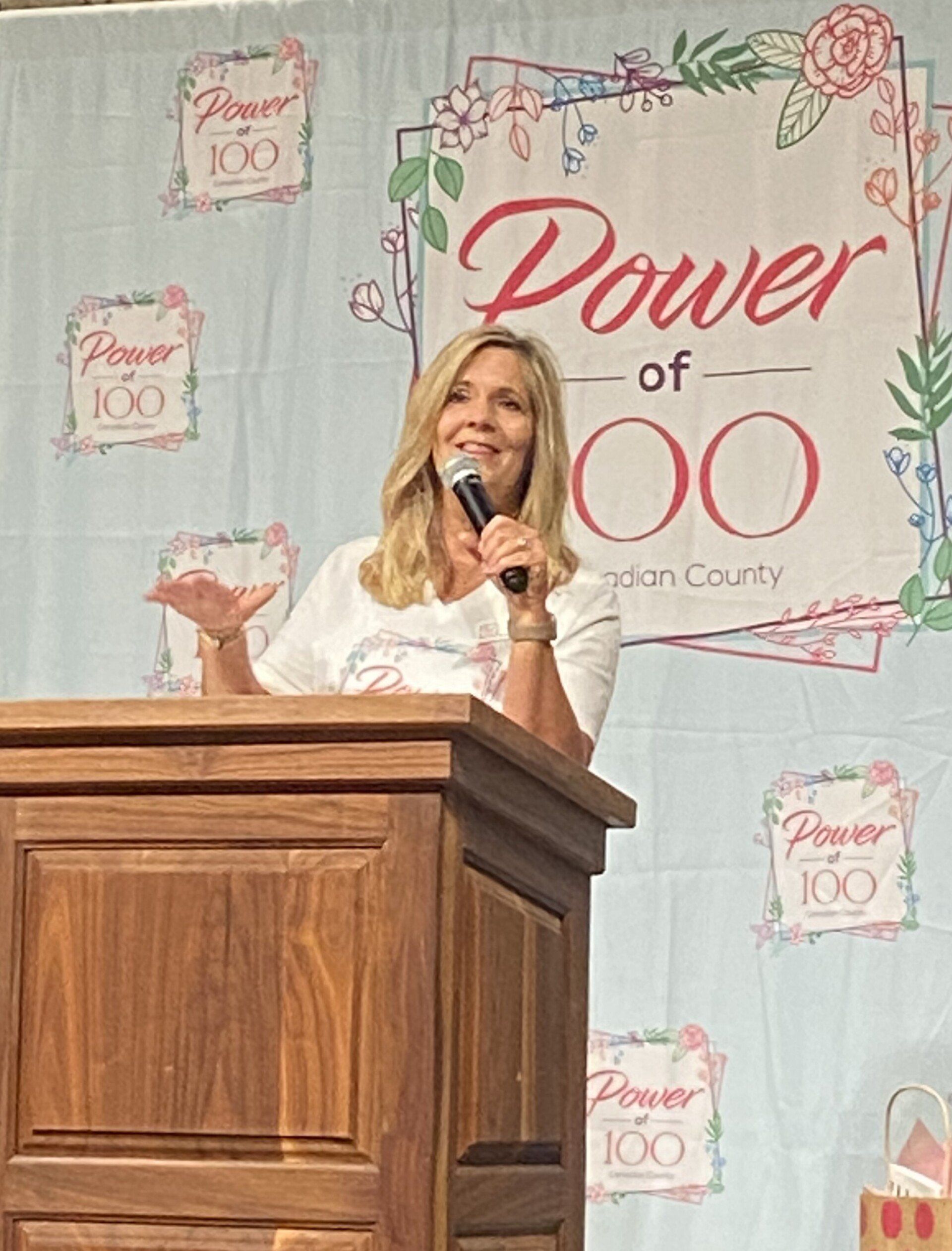 A woman is standing at a podium holding a microphone.