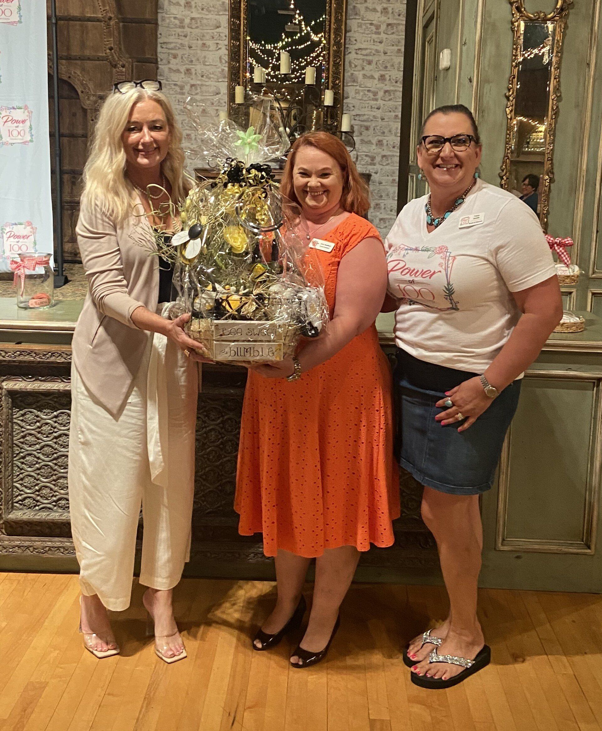Three women are standing next to each other holding a basket of flowers.