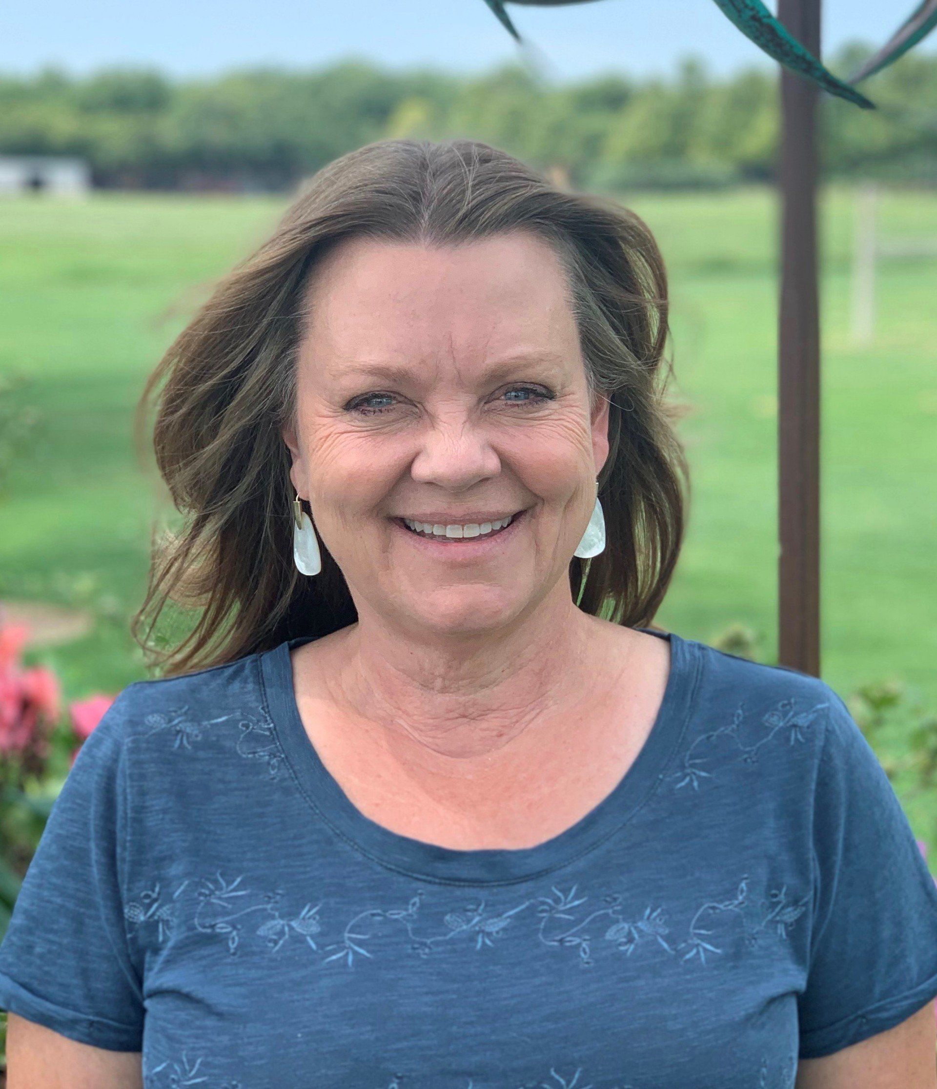 A woman wearing a blue shirt and earrings is smiling for the camera.