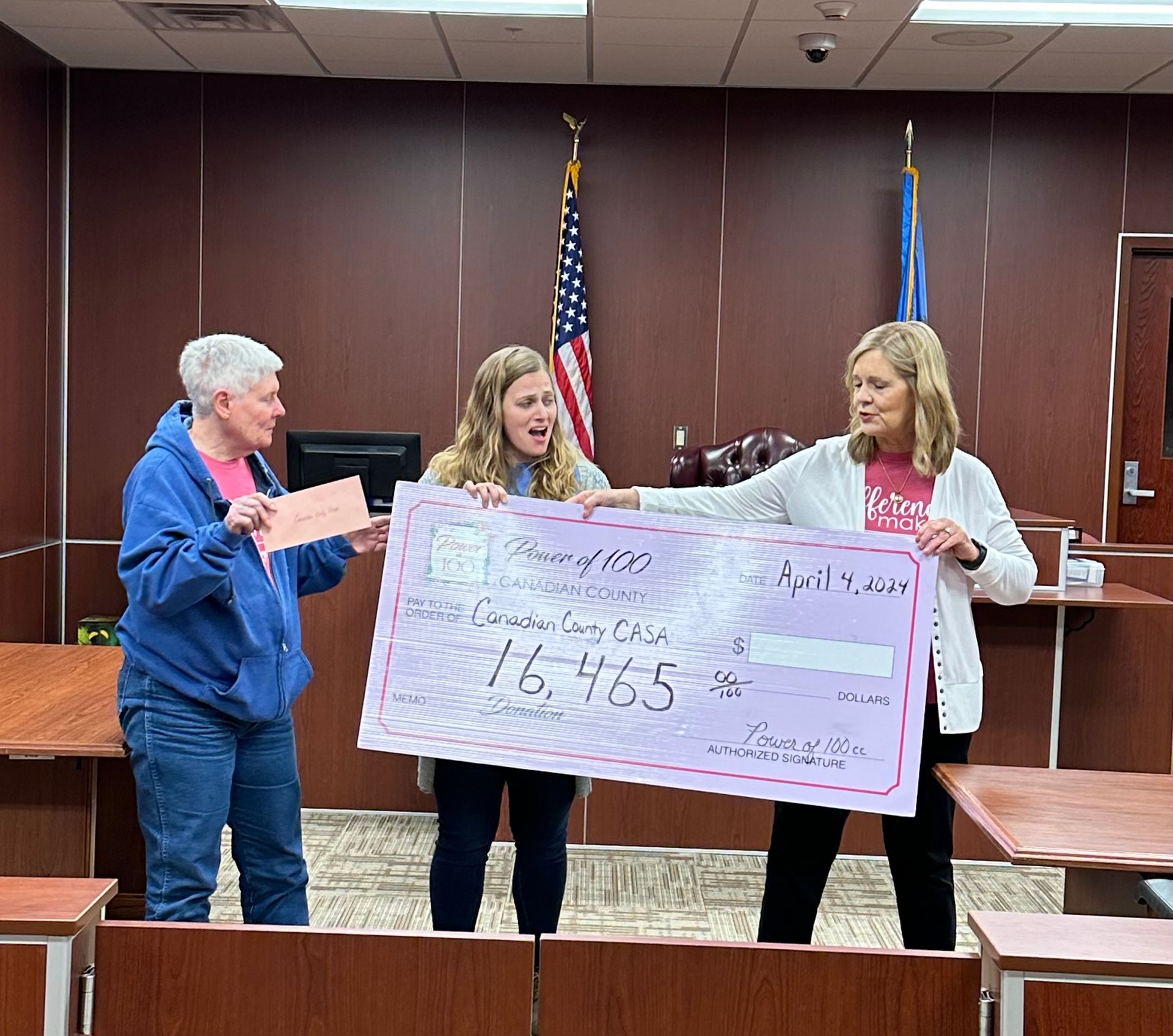 Three women are holding a large pink check in a courtroom.