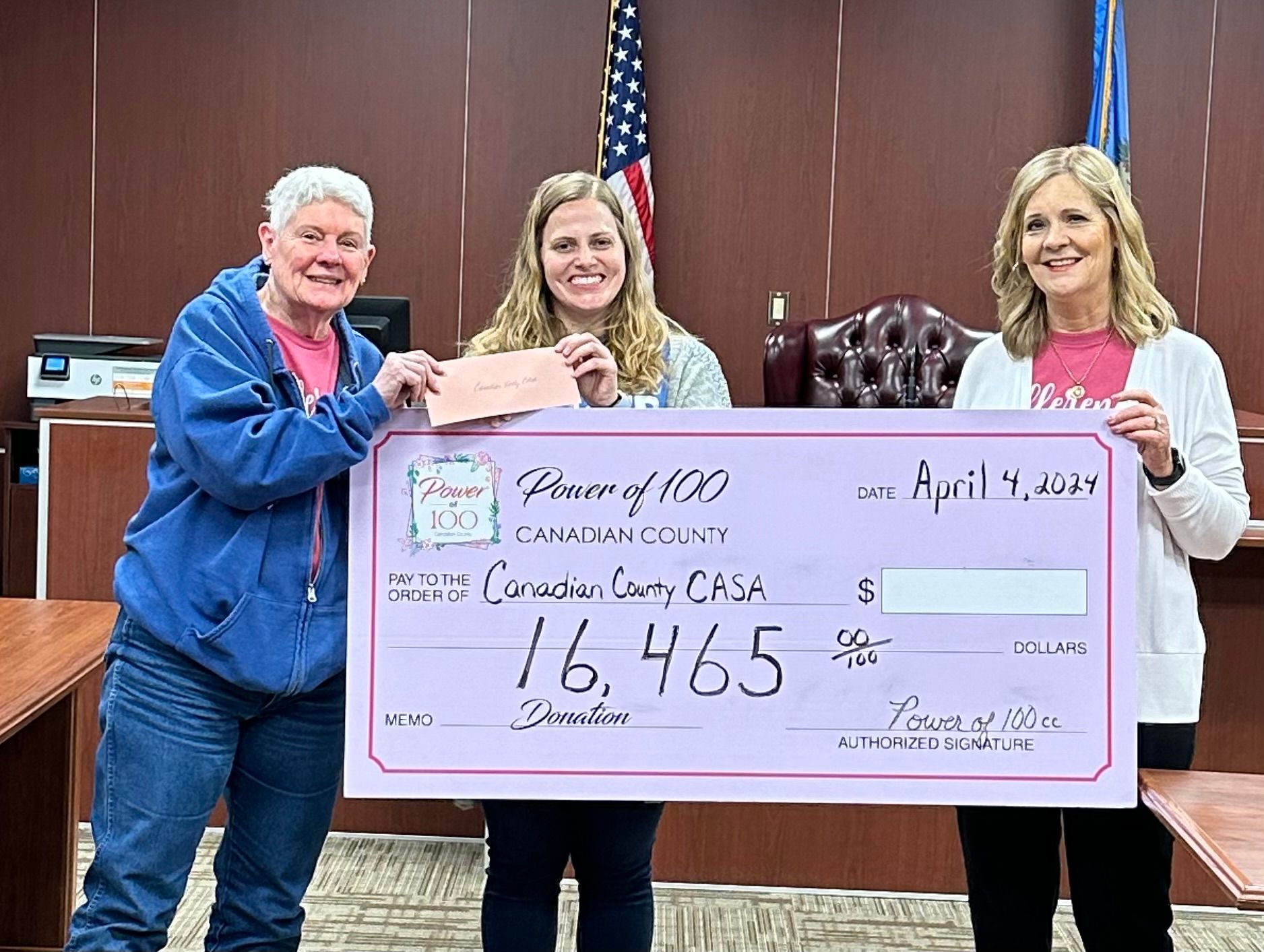Three women are holding a large check in a courtroom.