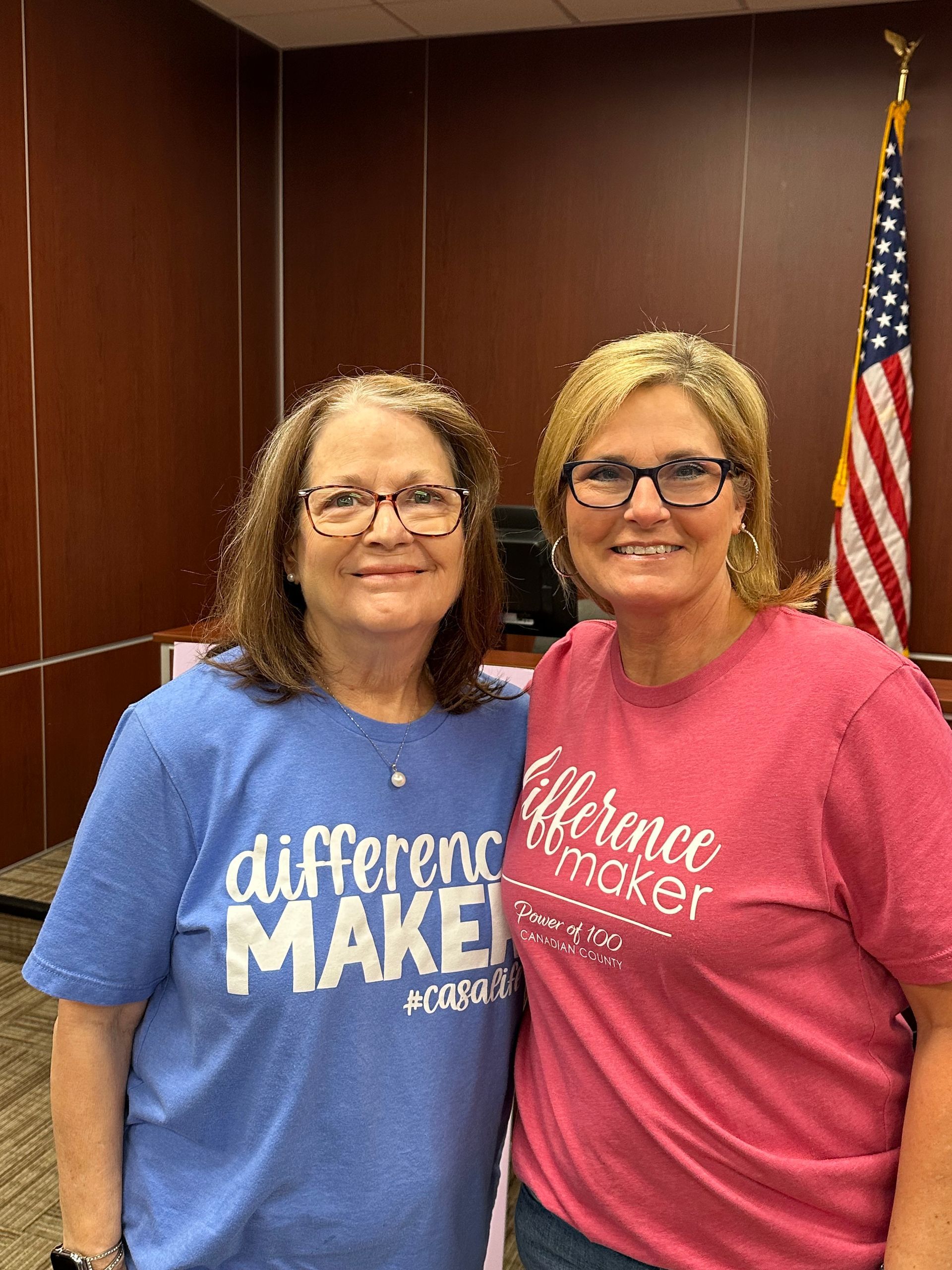 Two women are posing for a picture in front of an american flag.