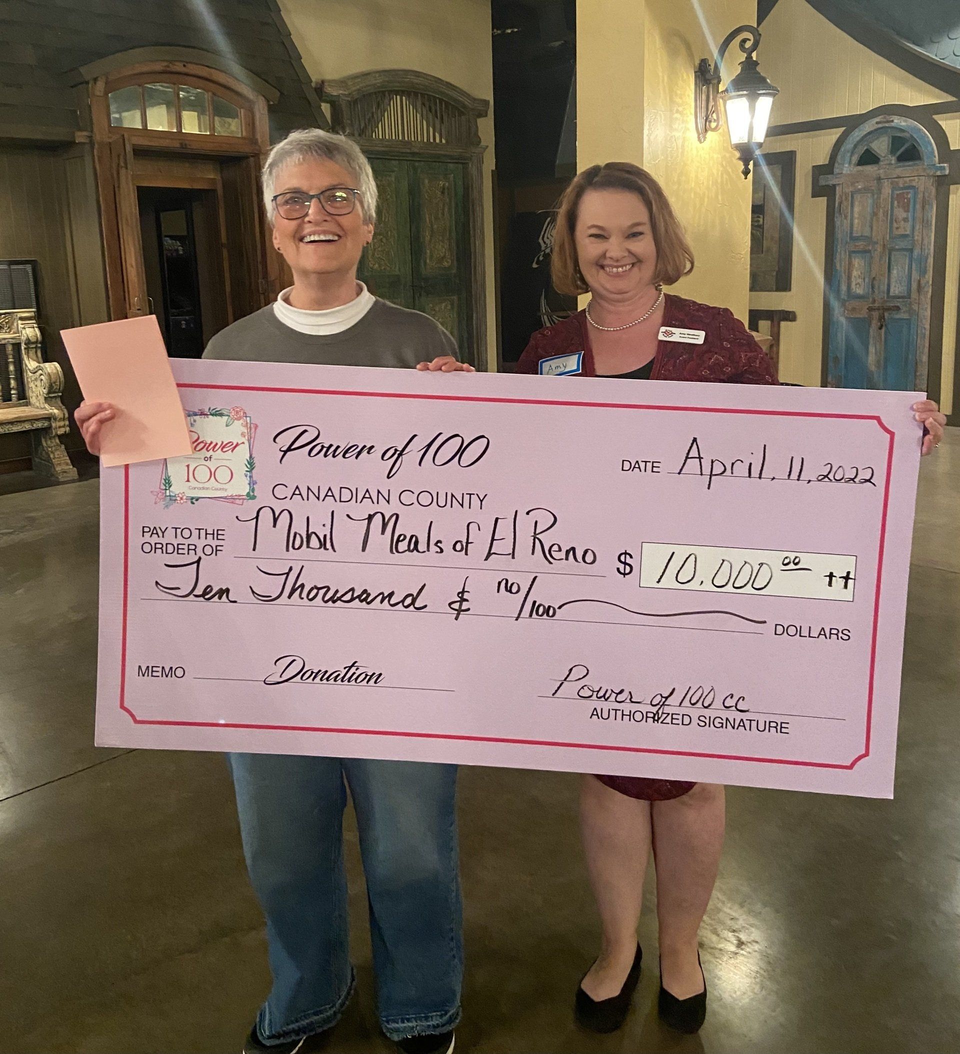 Two women holding a large pink check that says power of 100