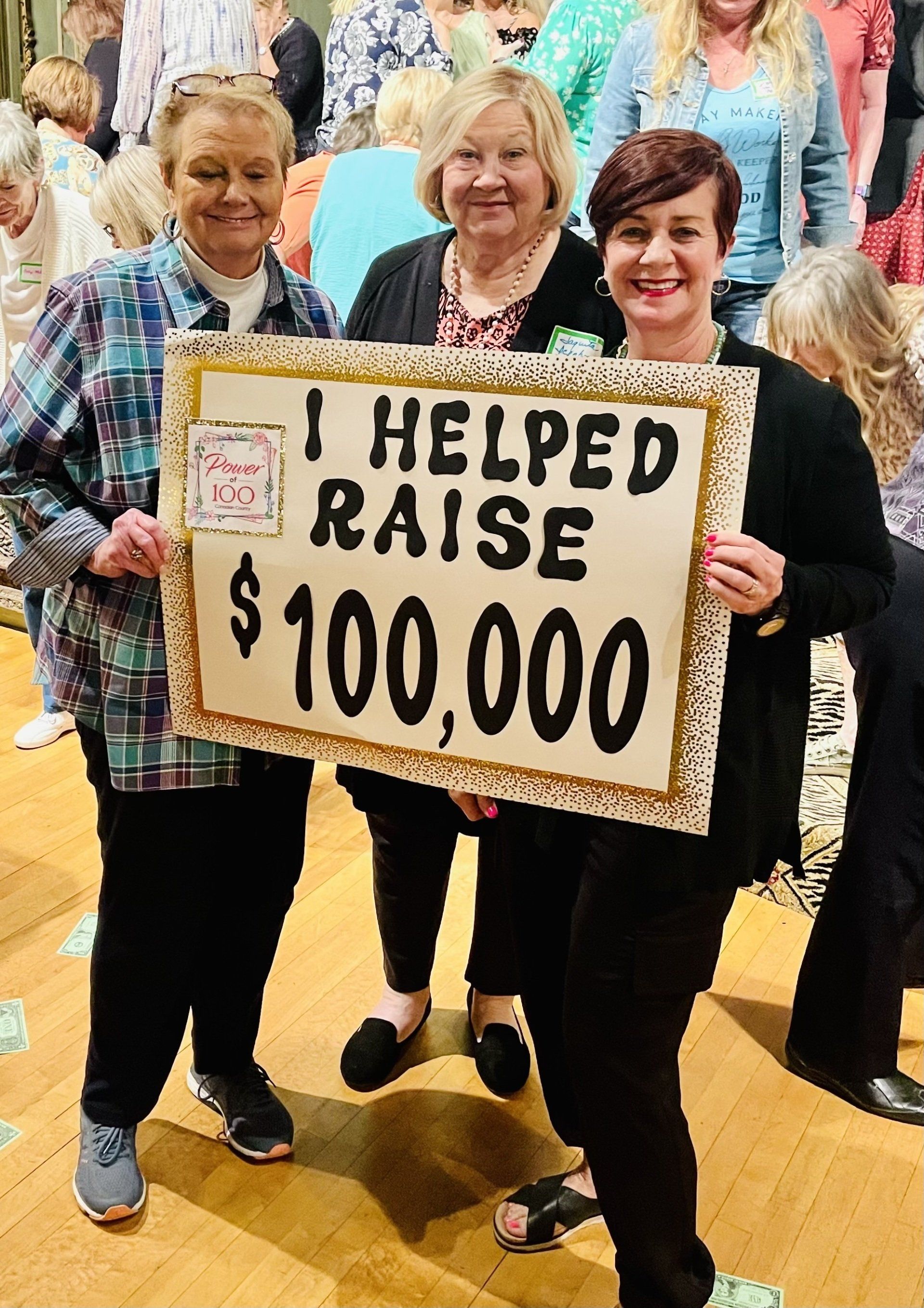 Three women are holding a sign that says `` i helped raise $ 100,000 ''.