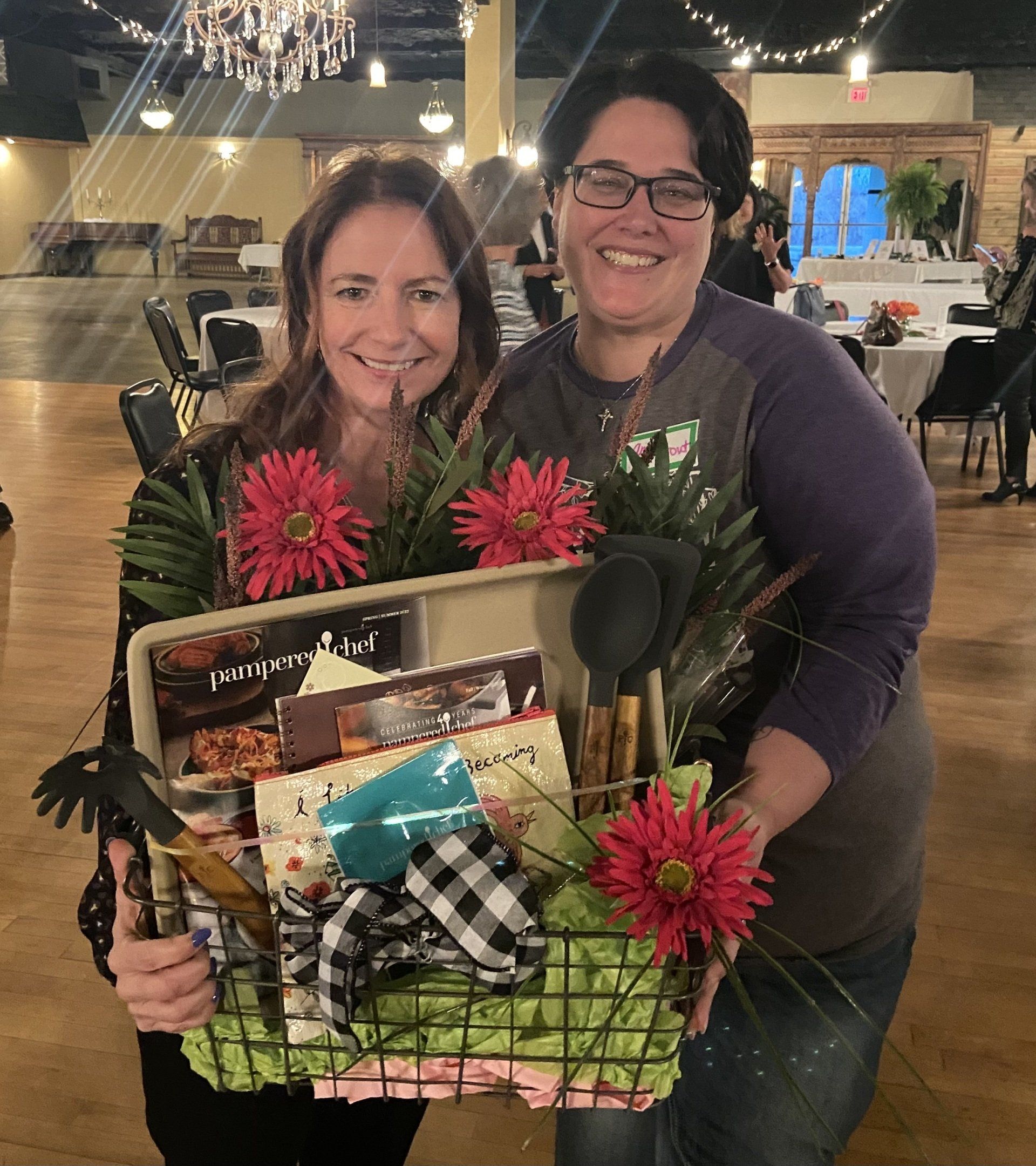 Two women are holding a basket of flowers and utensils