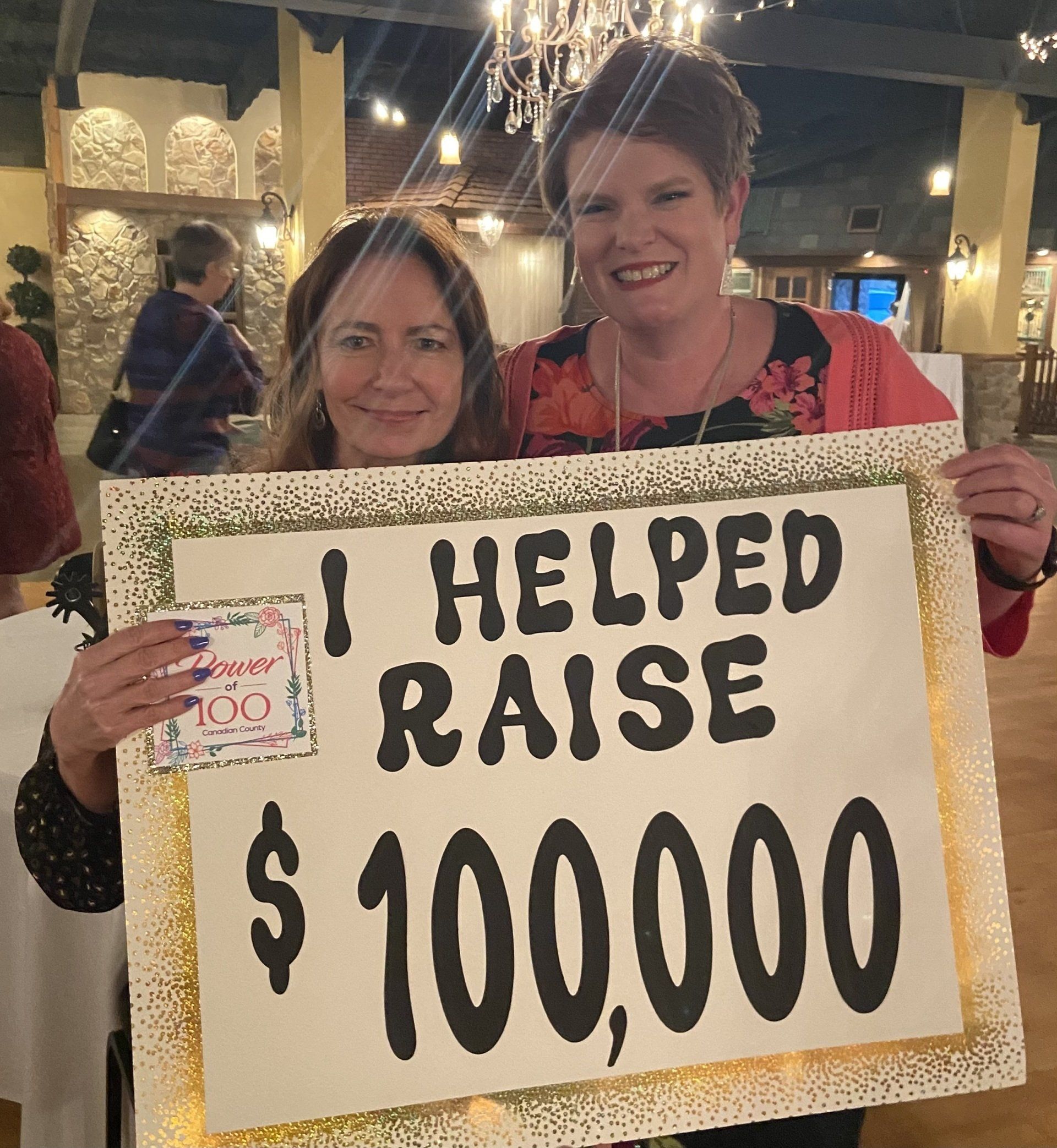Two women holding a sign that says i helped raise $ 100,000