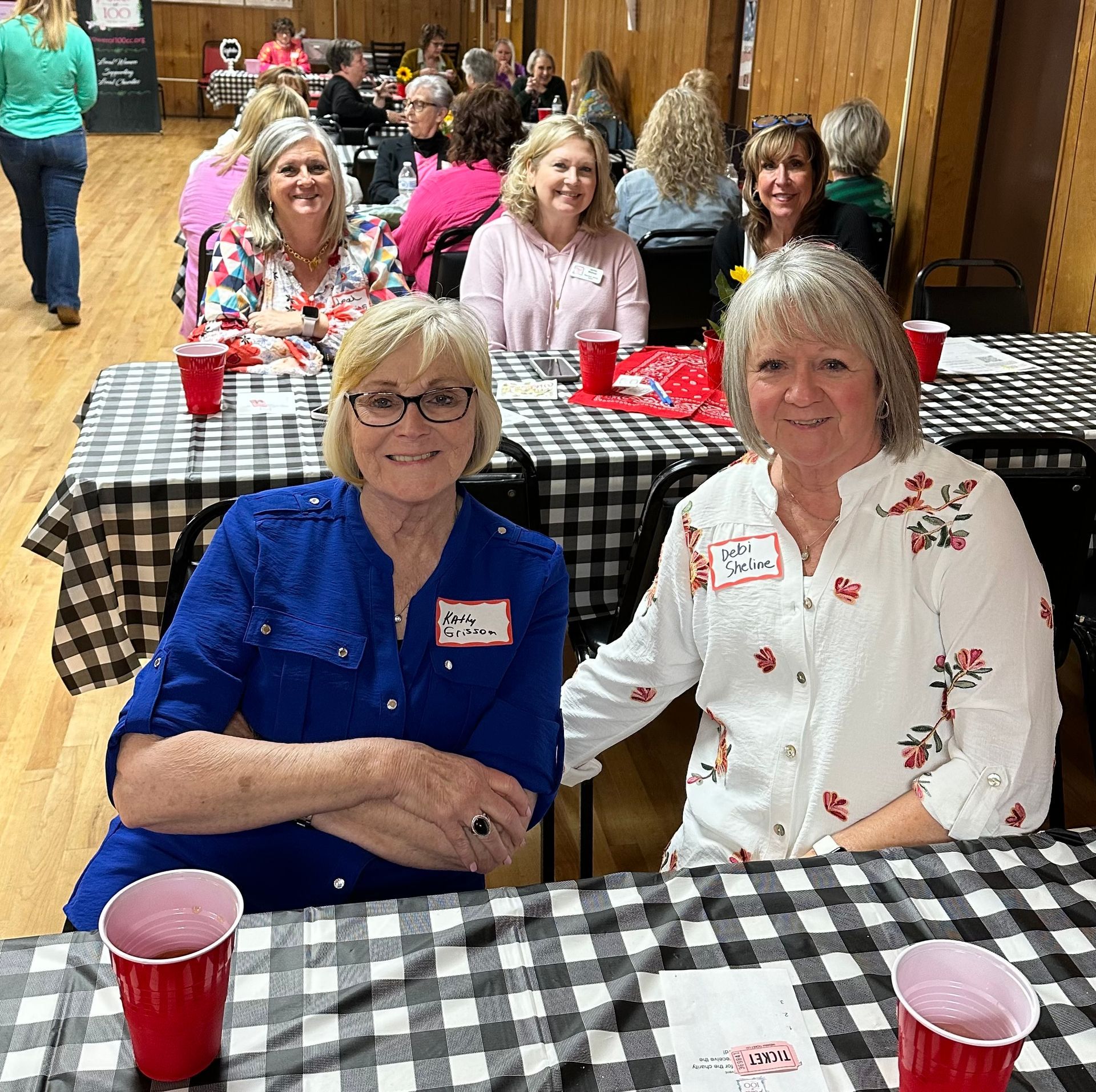 Two women are sitting at a table with a checkered tablecloth.