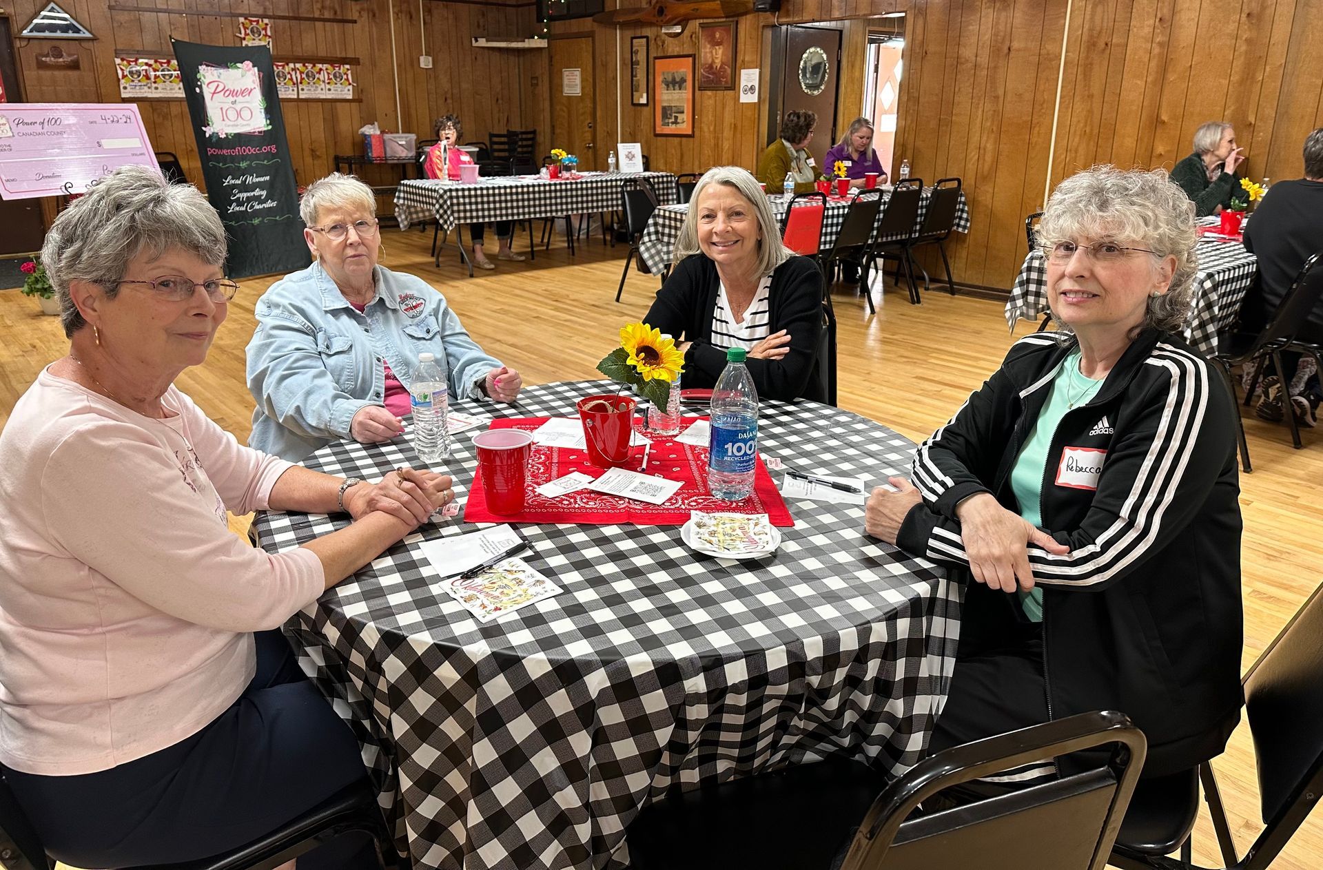 A group of women are sitting at a table with a checkered tablecloth.