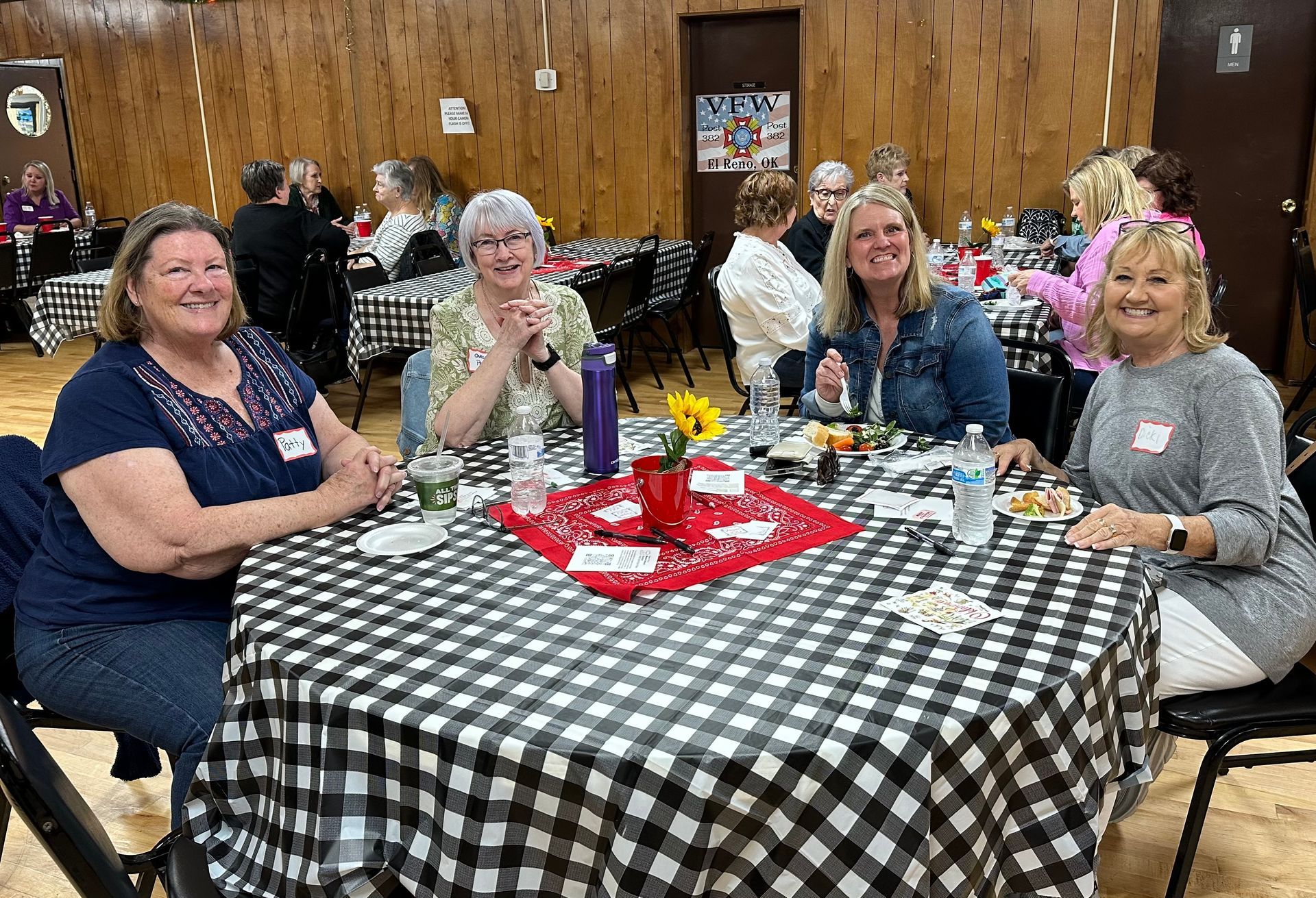 A group of women are sitting at a table with a checkered tablecloth.
