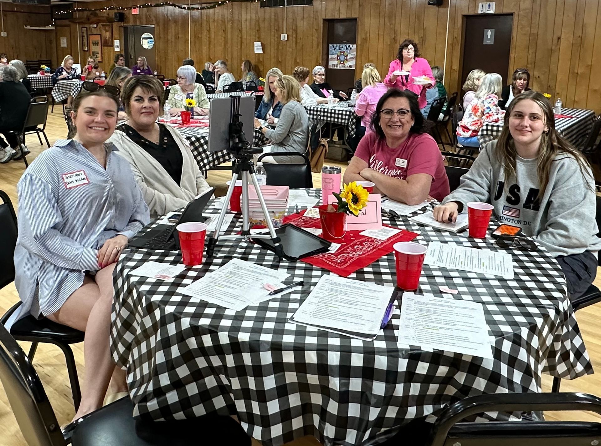A group of women are sitting at a table with a checkered tablecloth.