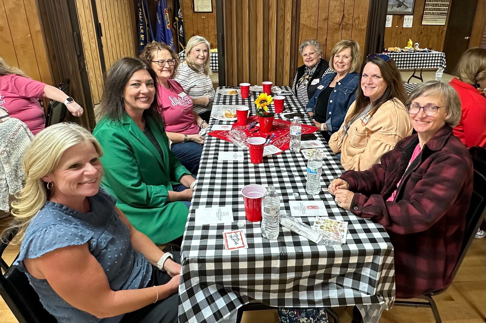 A group of women are sitting at a long table with a checkered tablecloth.