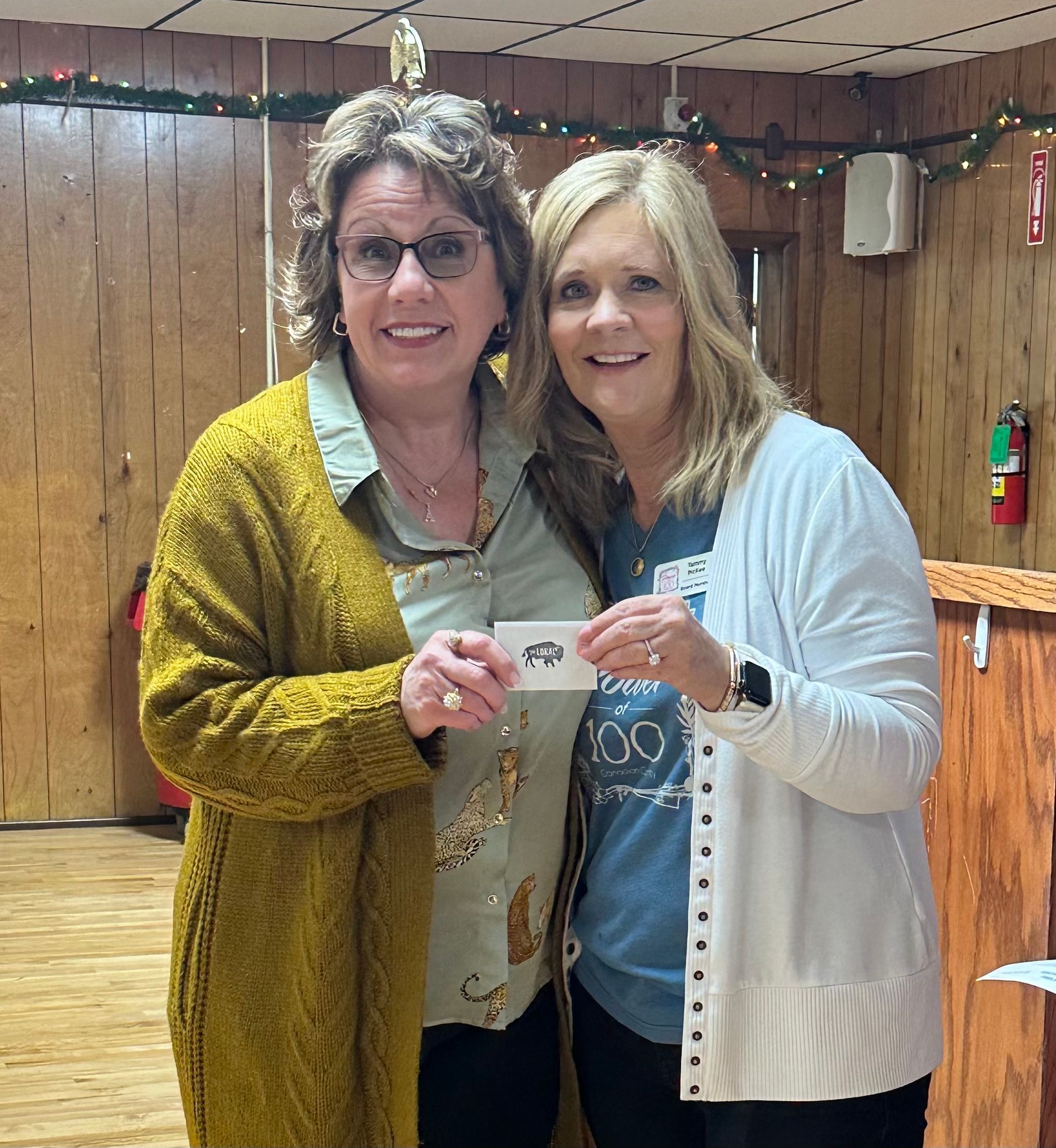 Two women are standing next to each other in a room holding a card.