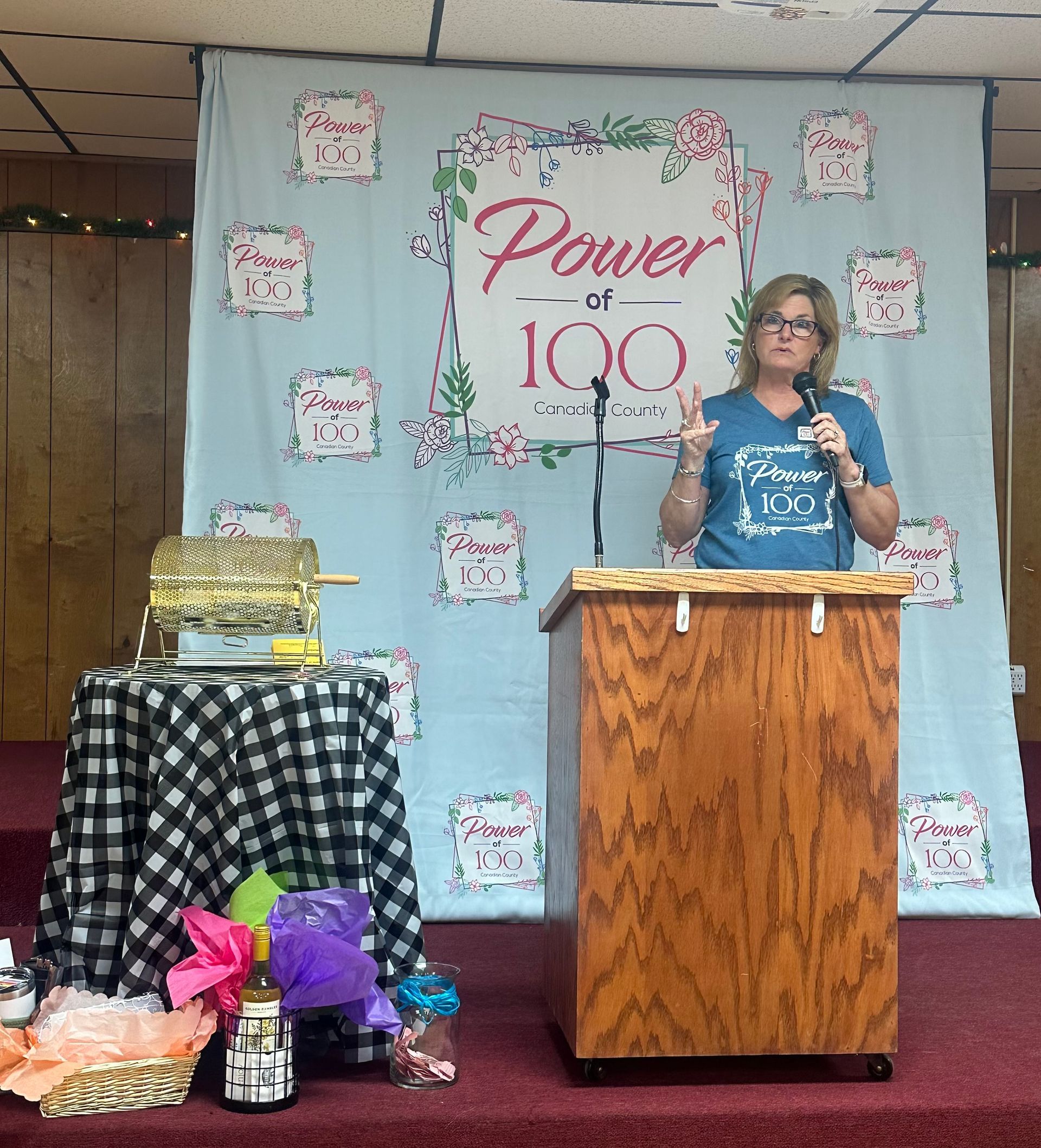 A woman stands at a podium in front of a sign that says power at 100