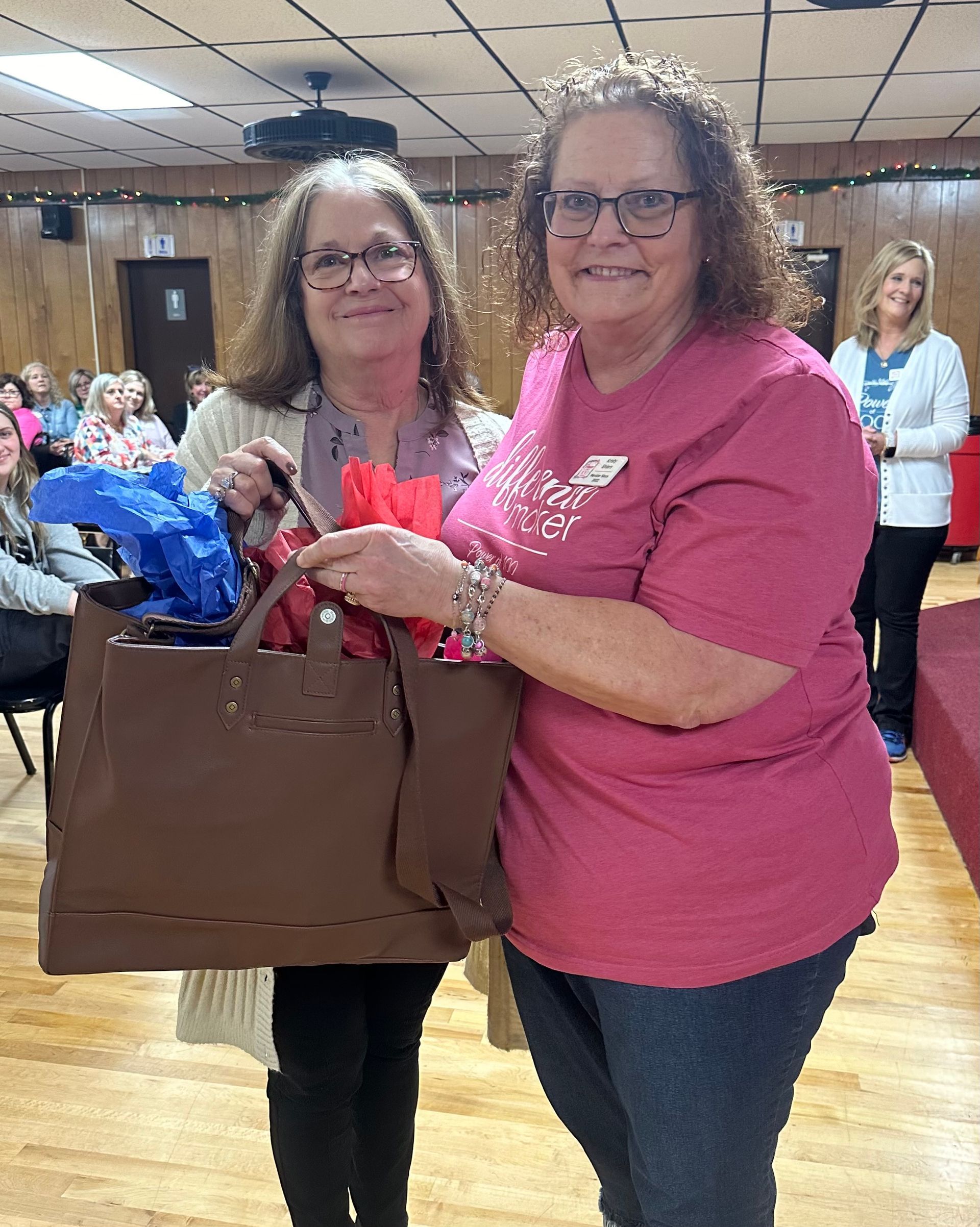 Two women are standing next to each other holding a brown bag.