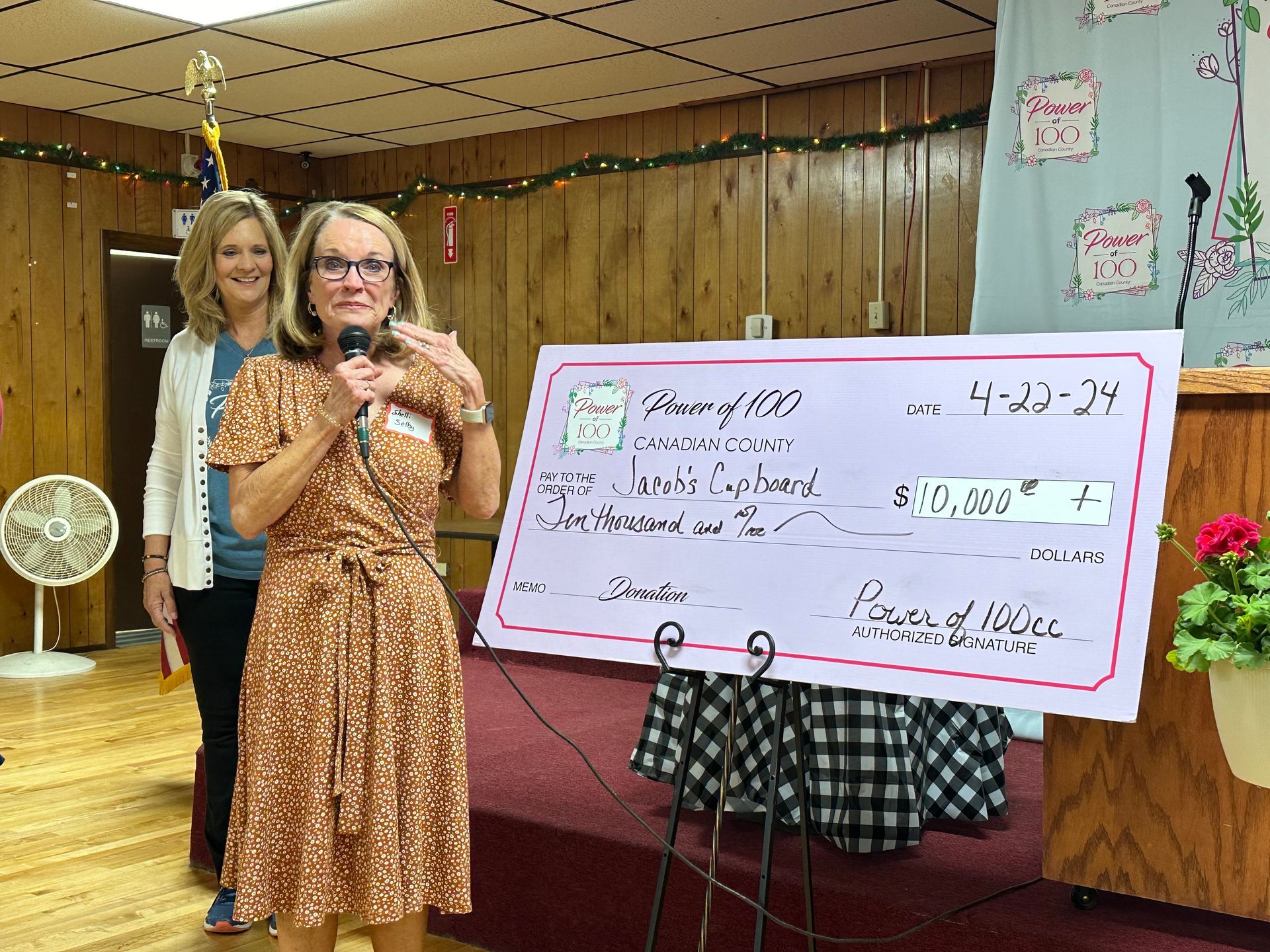 Two women are standing in front of a large check.
