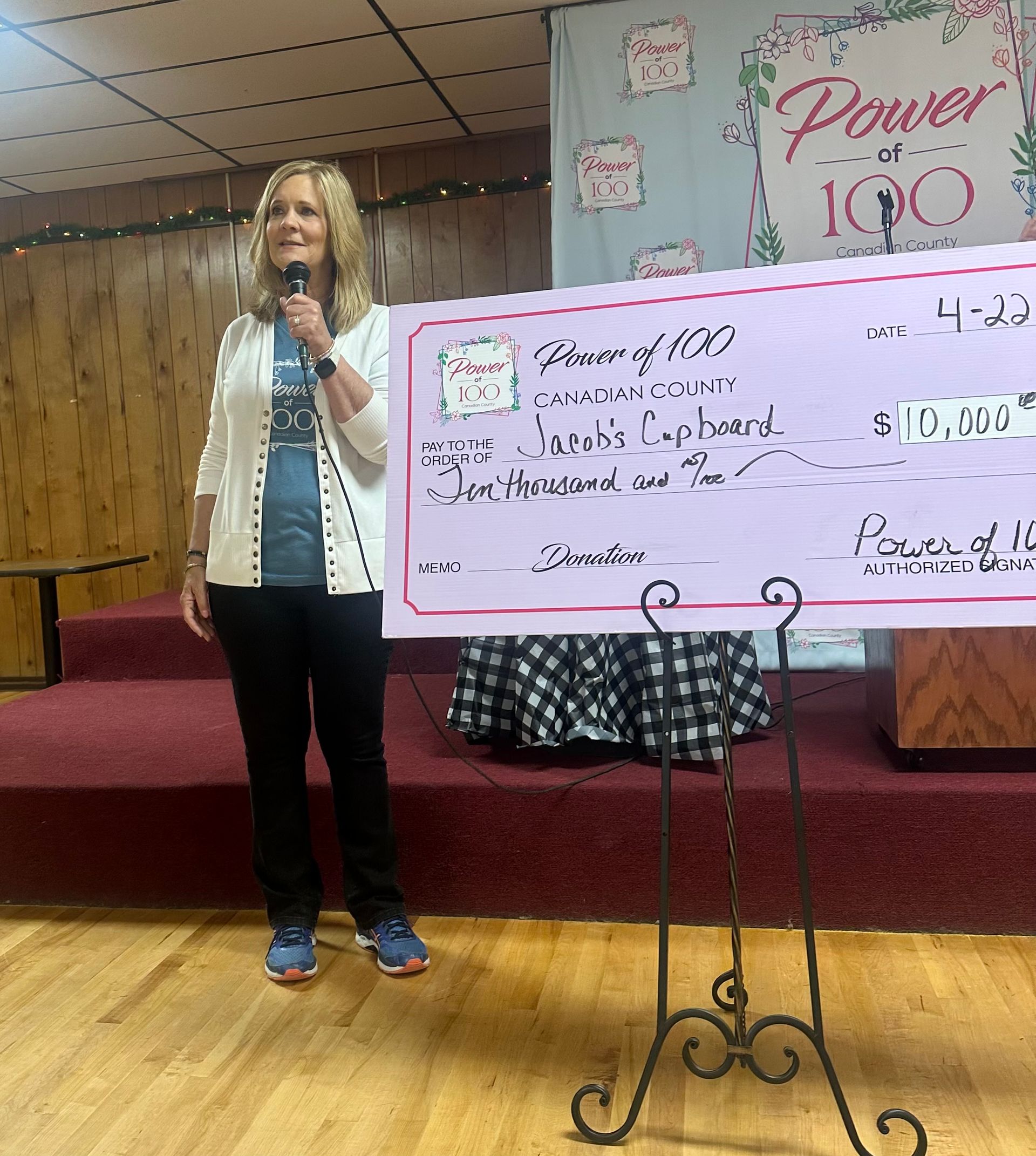A woman is standing on a stage holding a microphone in front of a large check.