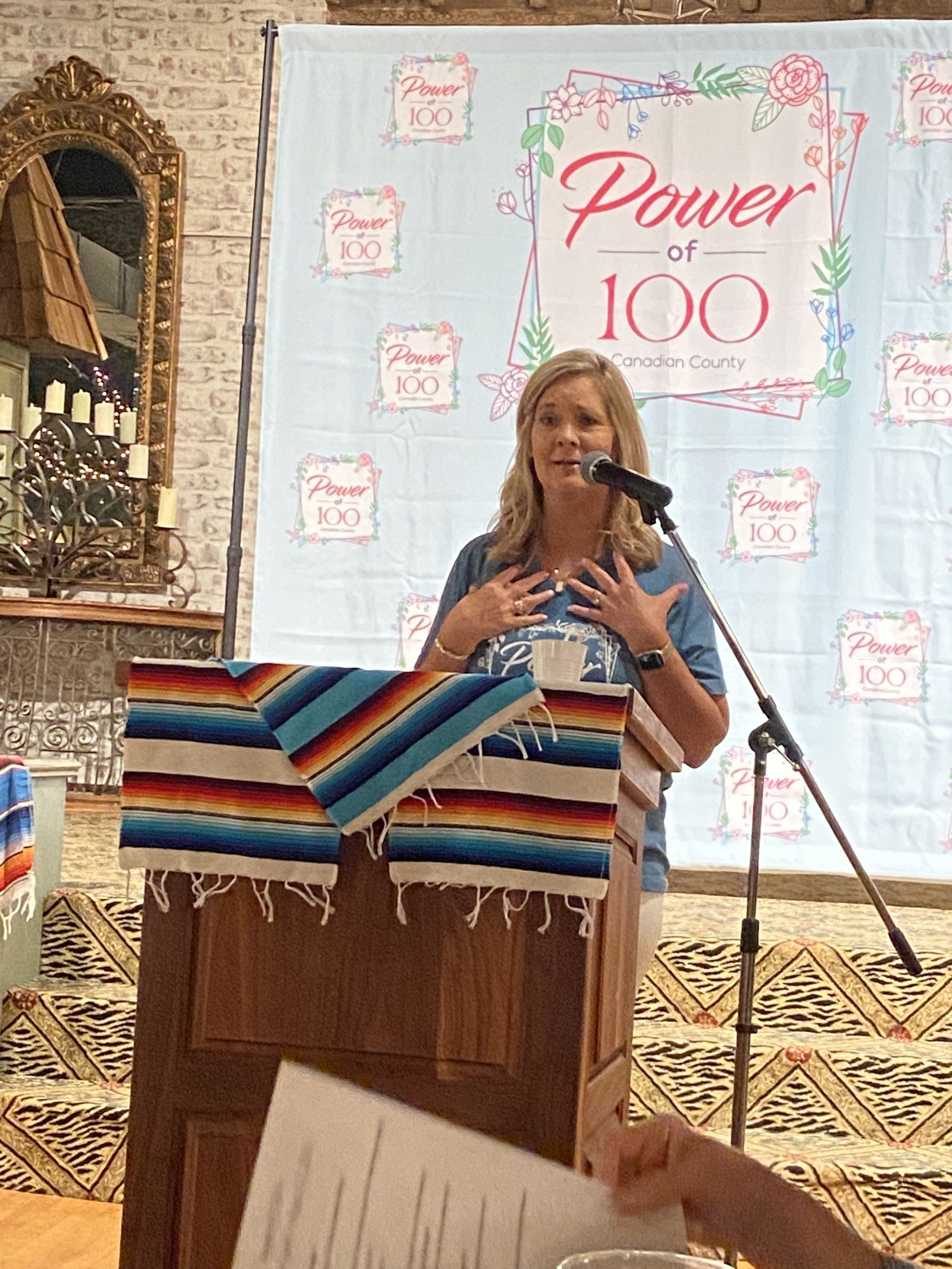 A woman stands at a podium with a sign behind her that says power of 100