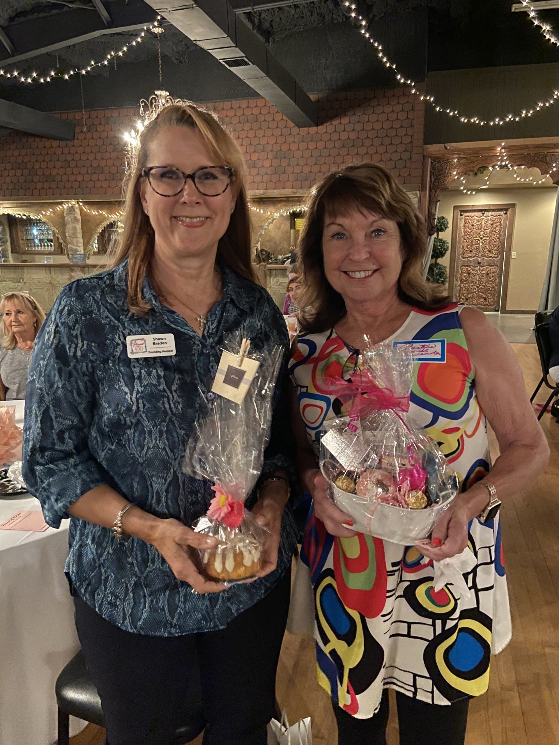 Two women are standing next to each other holding baskets of food.