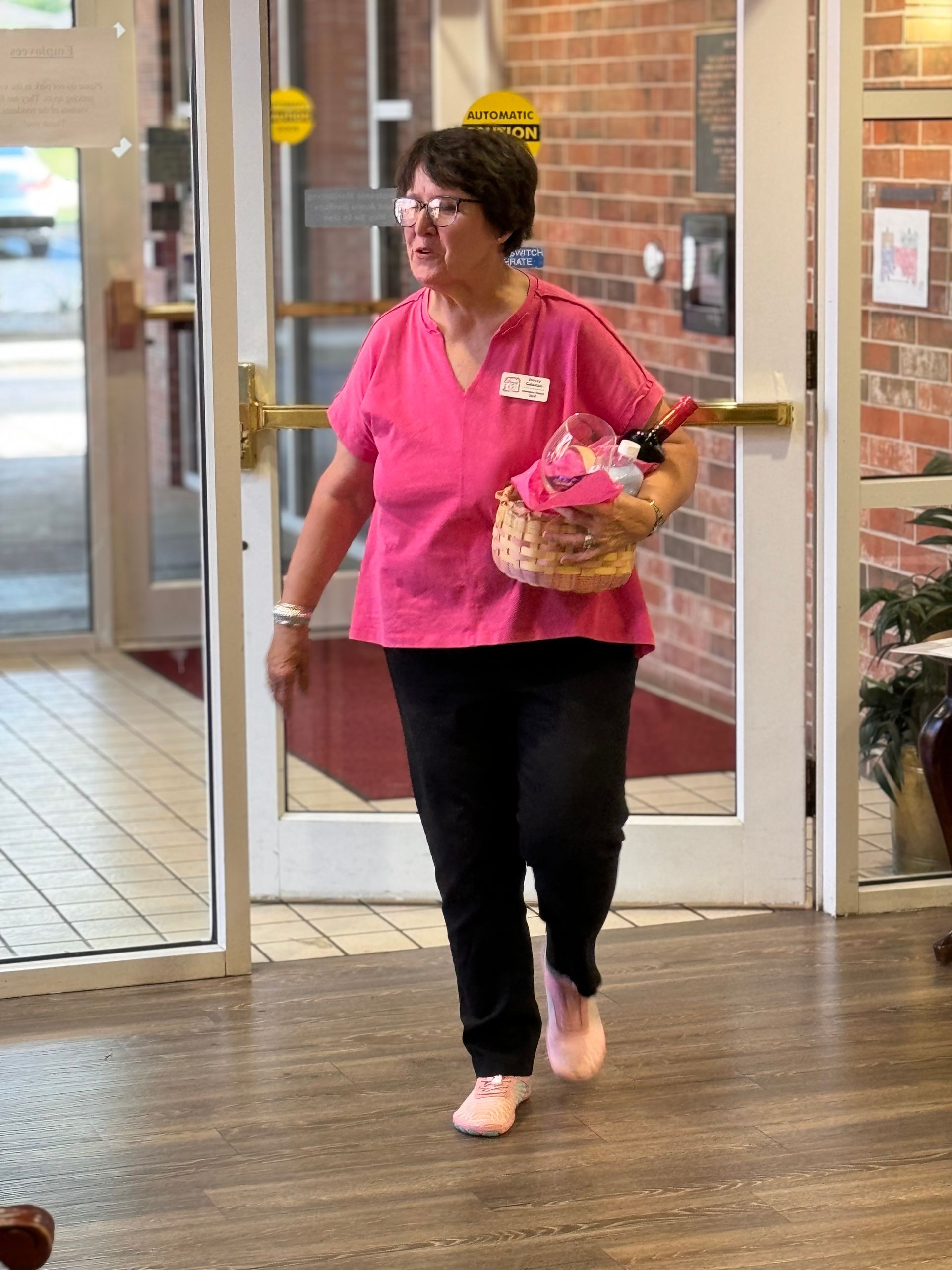A woman in a pink scrub top is walking through a door holding a basket.