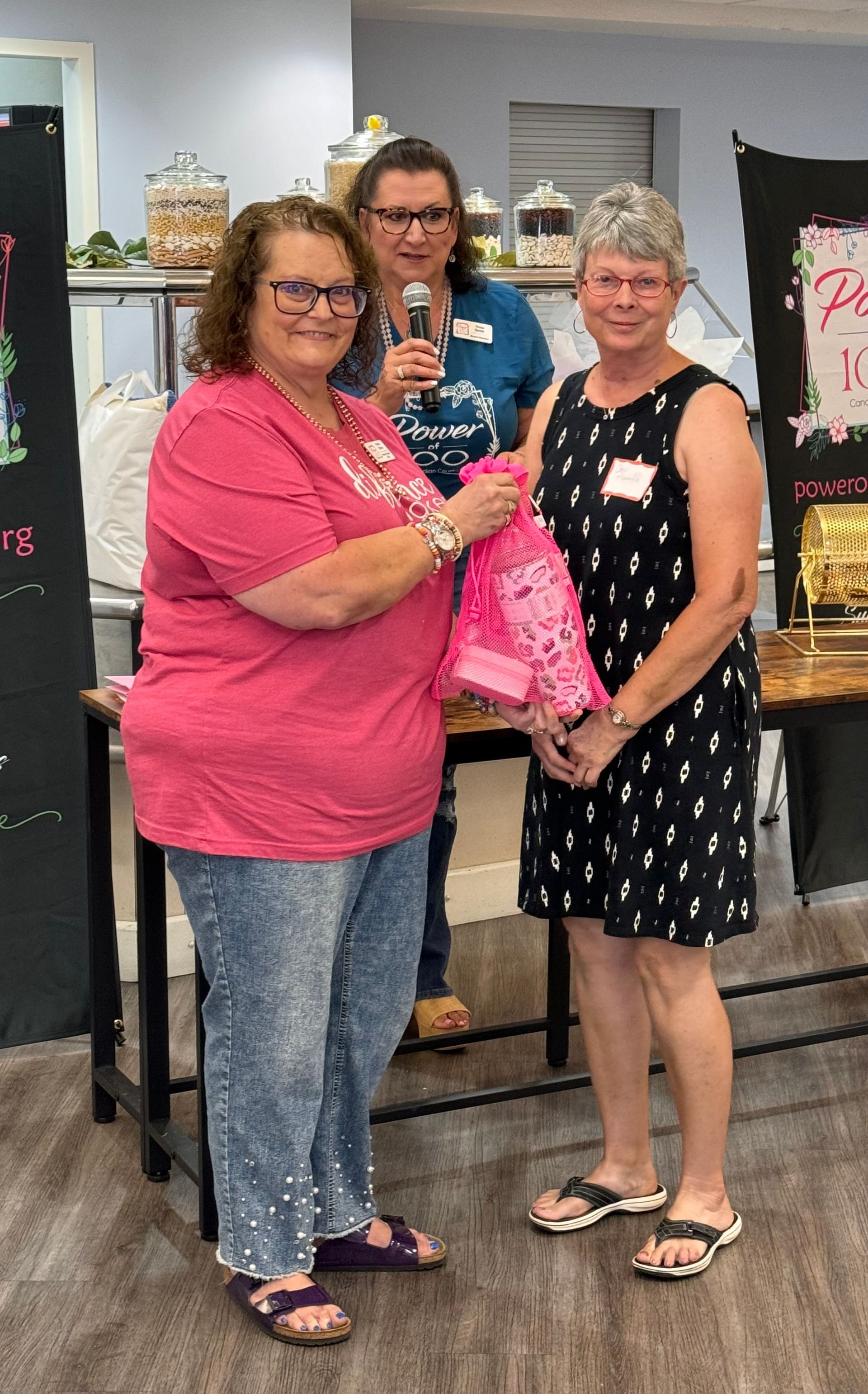 Three women are standing next to each other in a room holding a pink jacket.