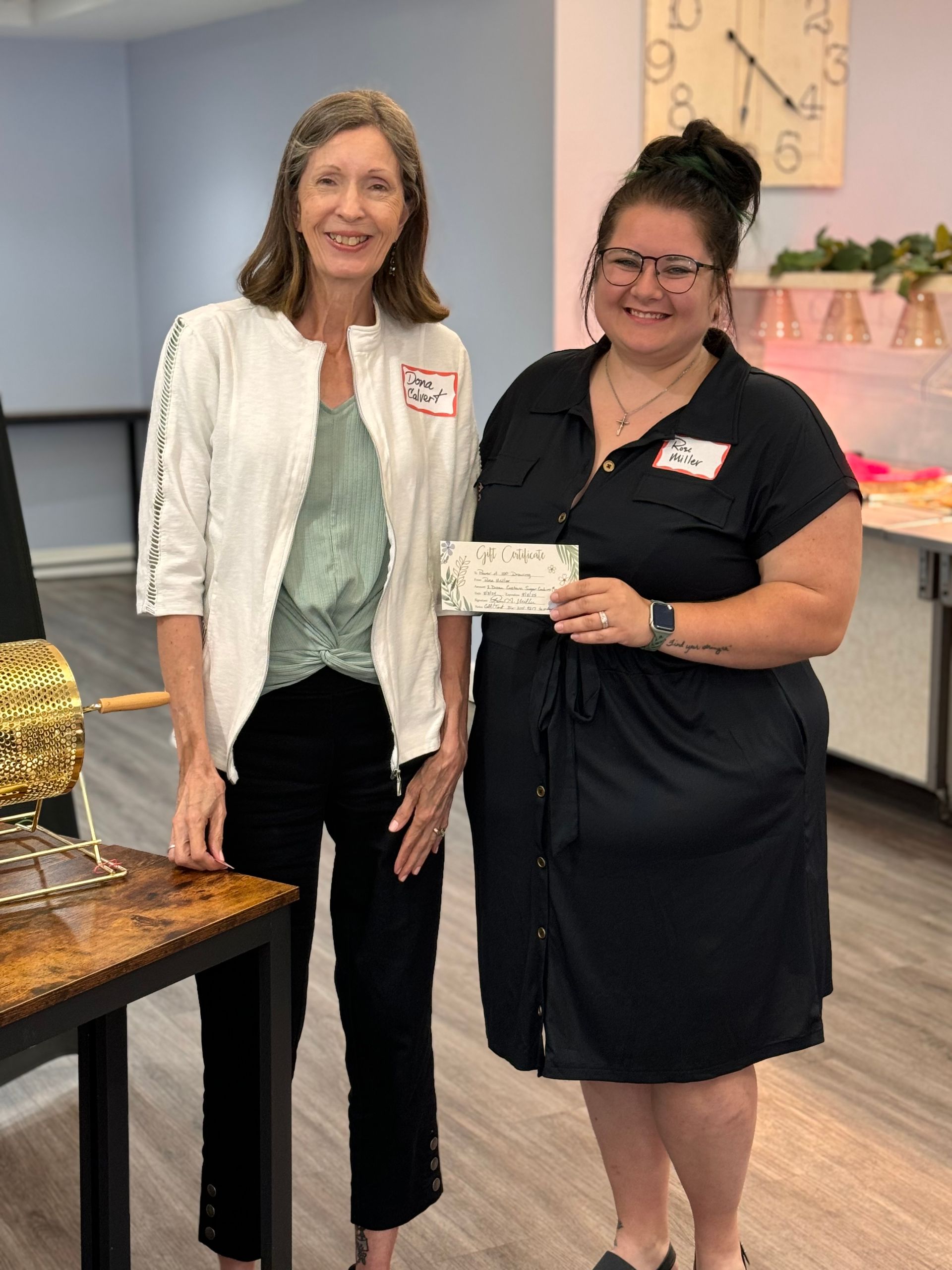 Two women are standing next to each other in a room holding a check.