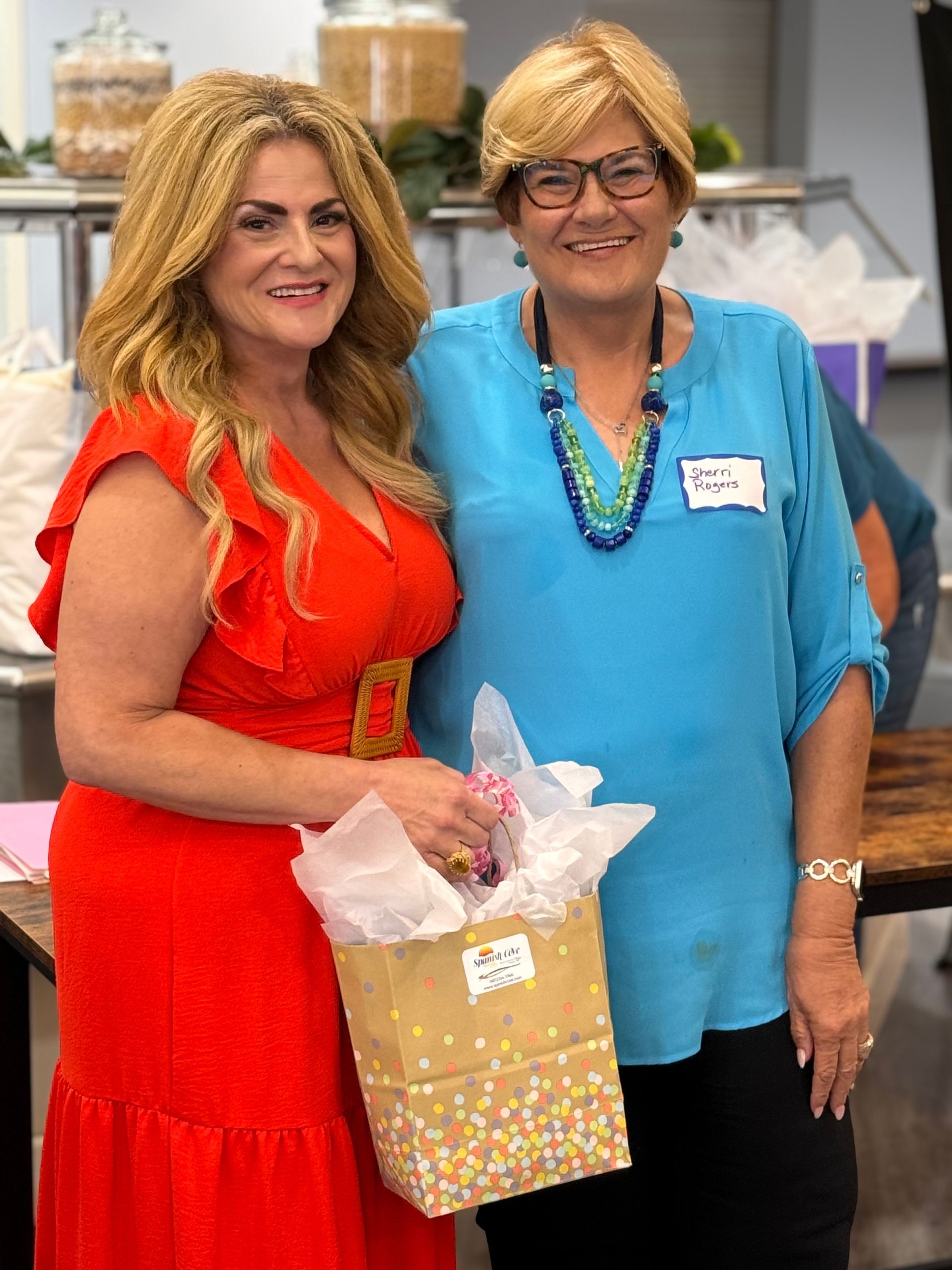 Two women are standing next to each other holding bags of tissue paper.