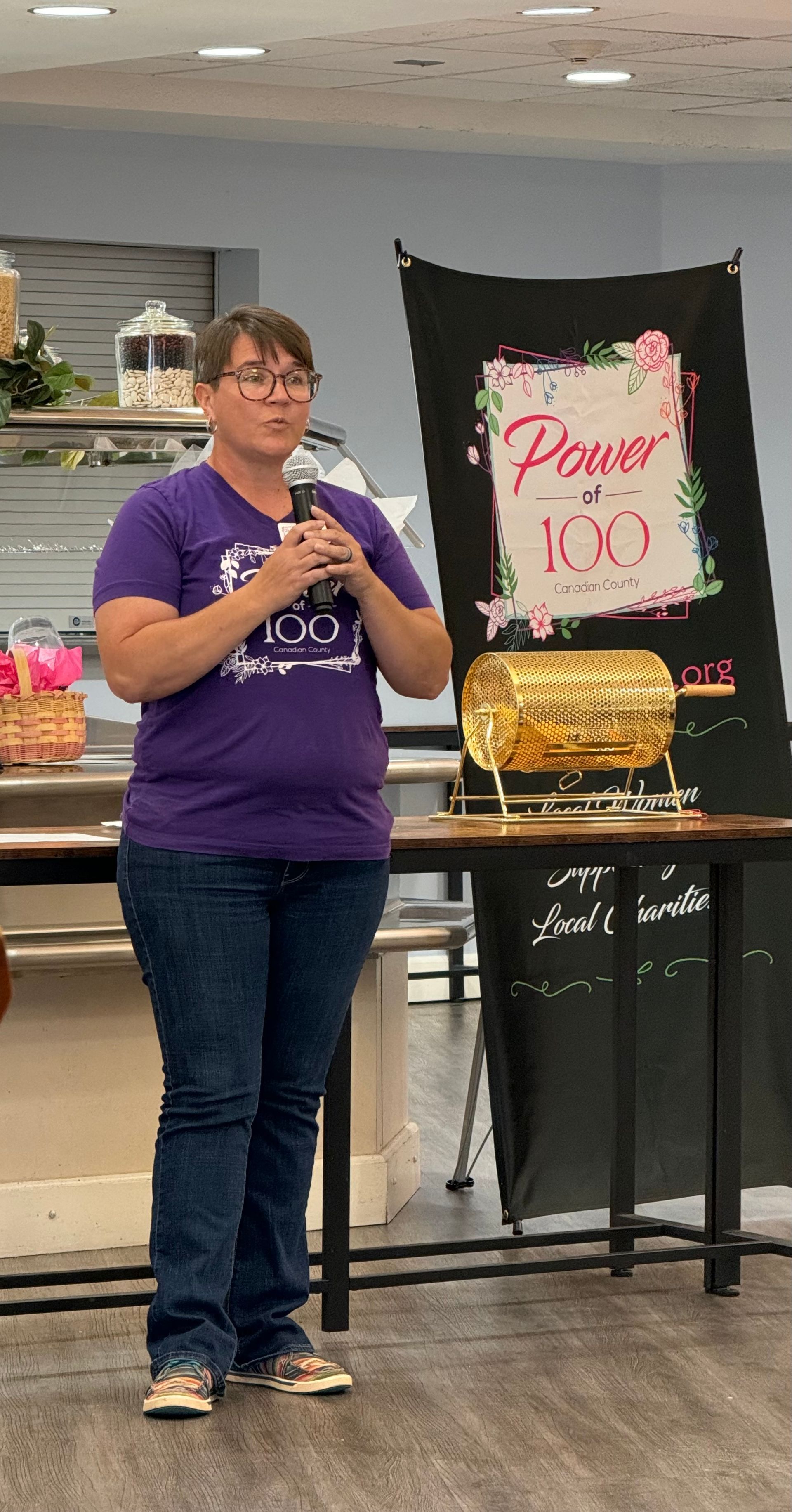 A woman in a purple shirt is standing in front of a microphone.
