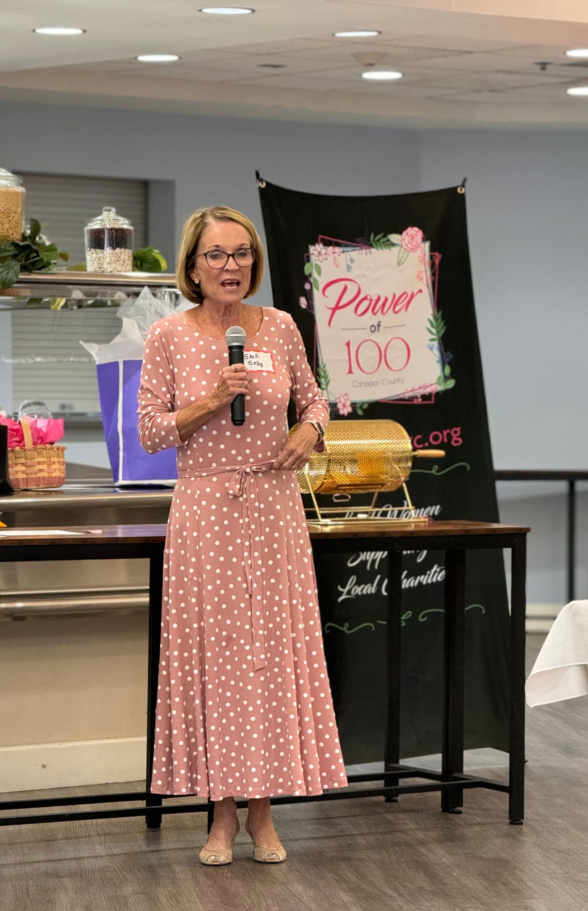 A woman in a pink polka dot dress is standing in front of a microphone.
