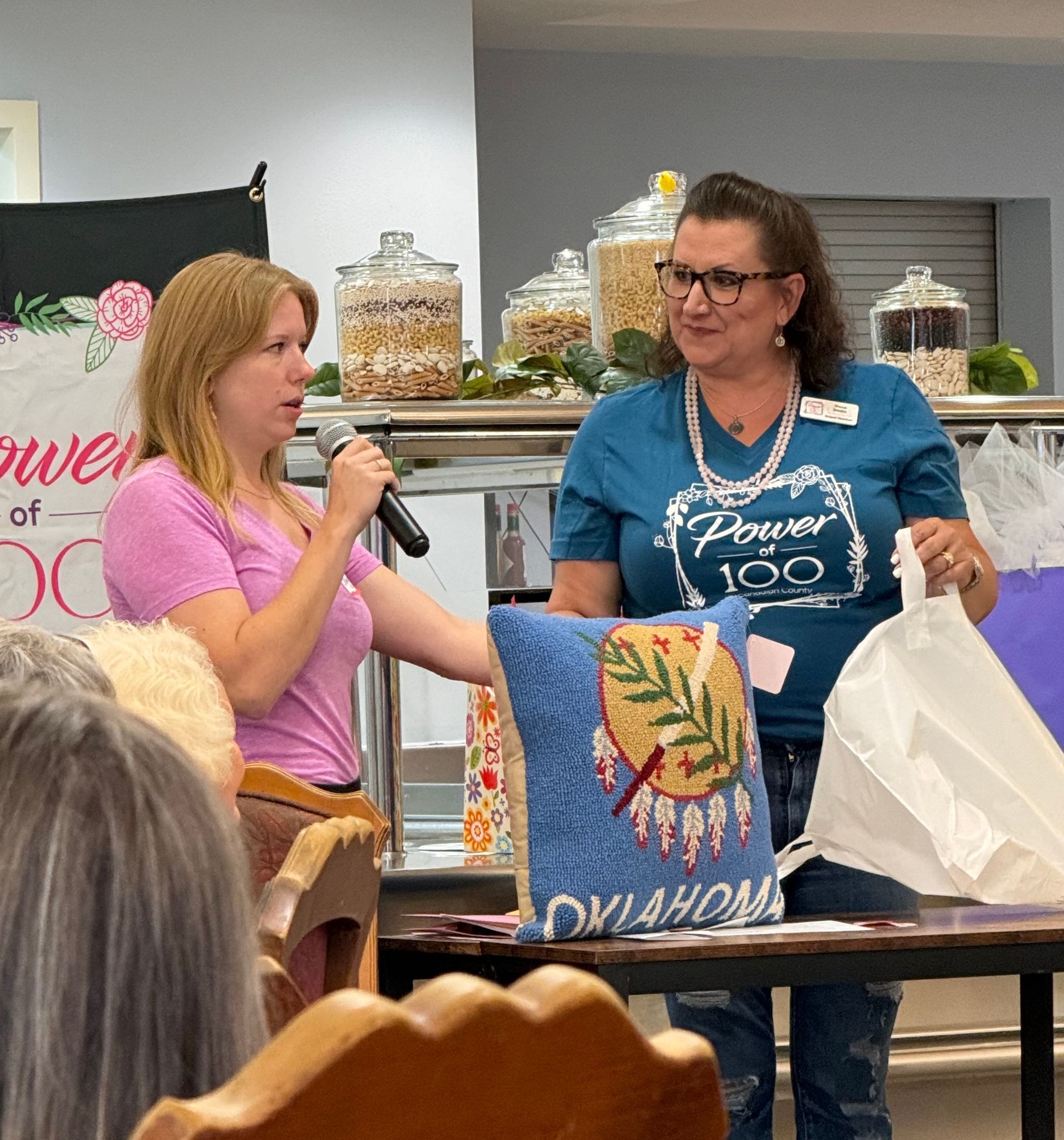 A woman in a blue shirt that says power 100 is speaking into a microphone