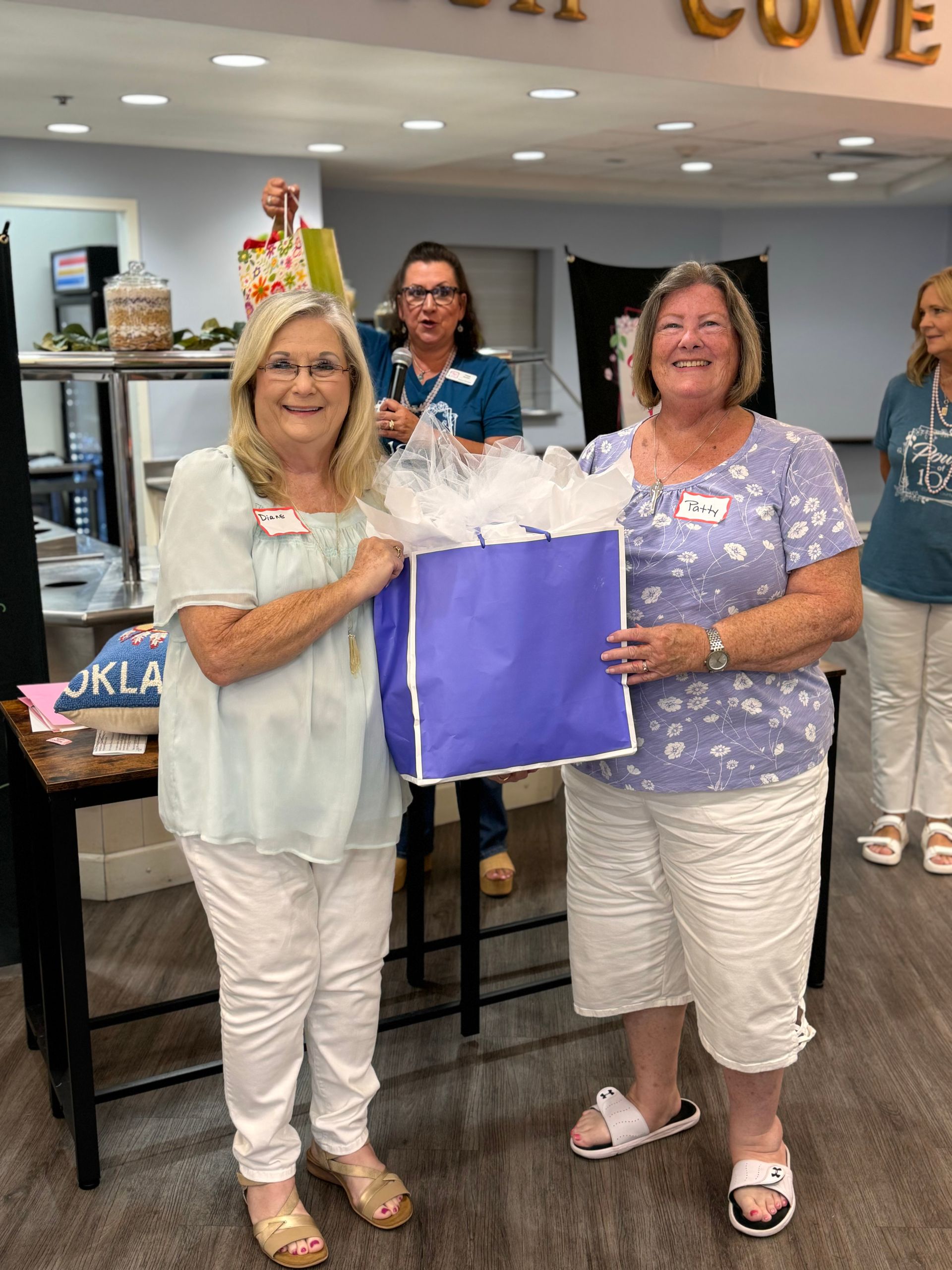 Two women are standing next to each other holding a purple bag.