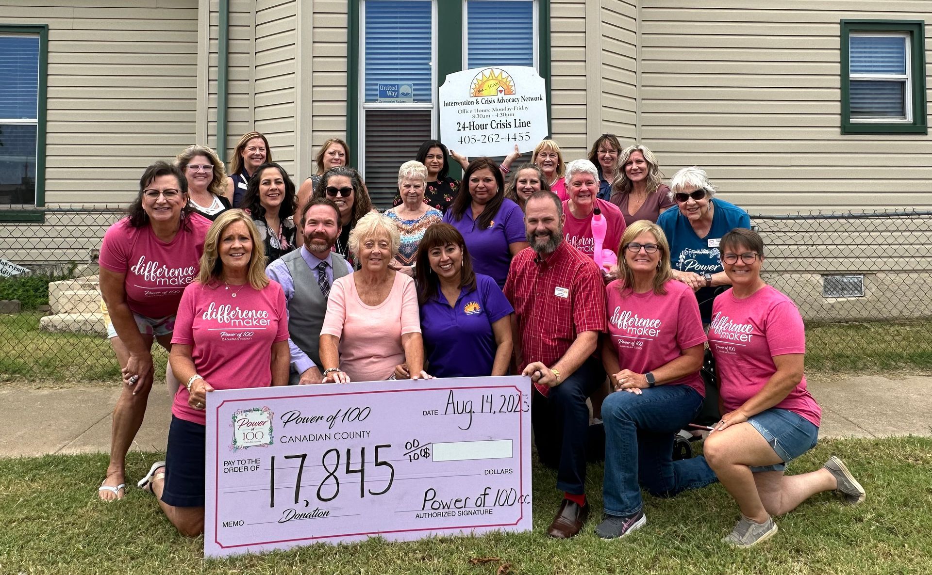 A group of people standing in front of a house holding a check.