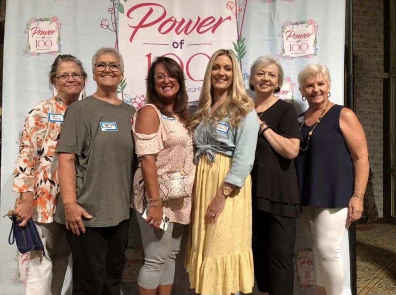 A group of women are posing for a picture in front of a power of 100 banner.