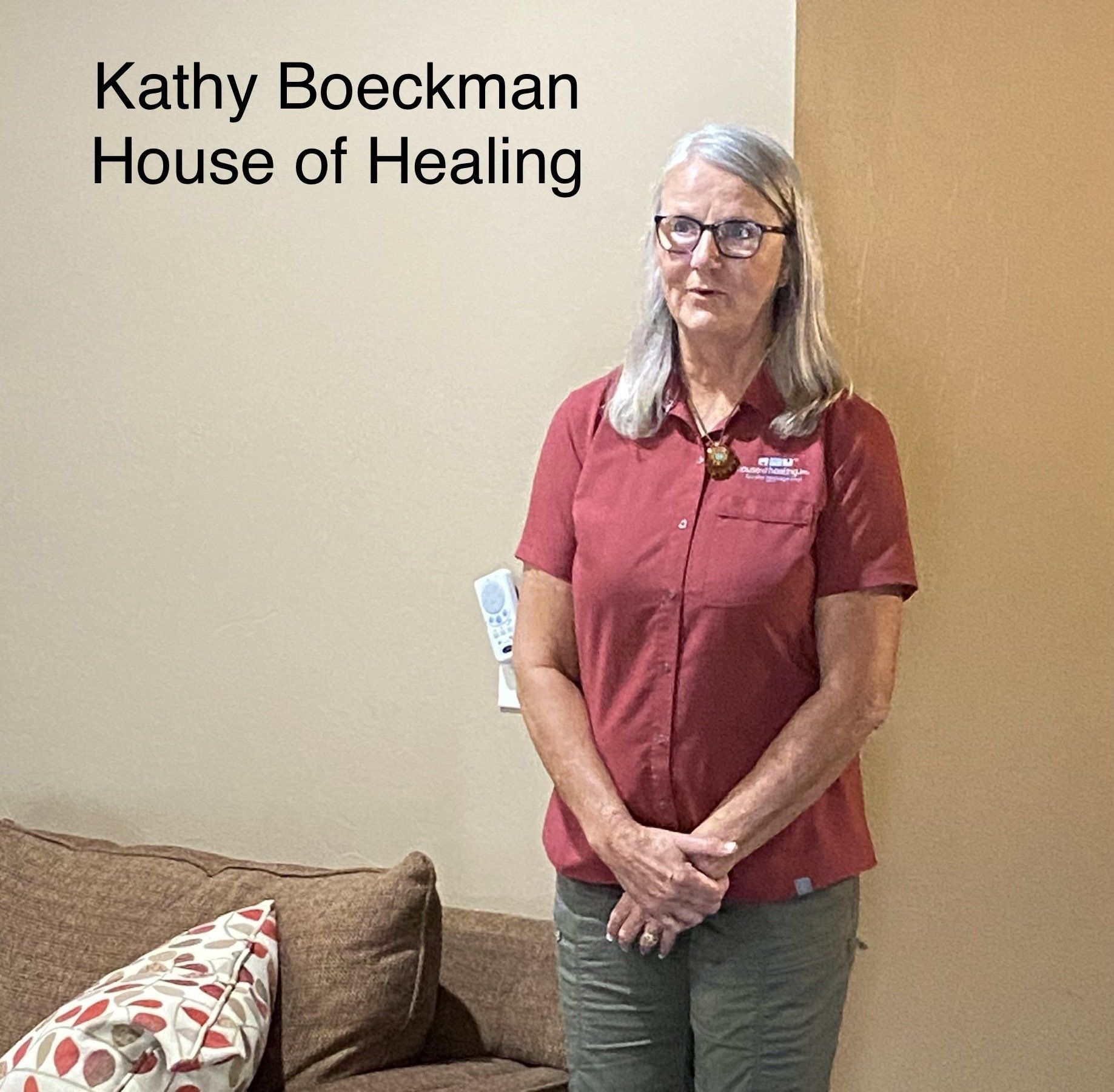 A woman in a red shirt is standing in front of a couch.