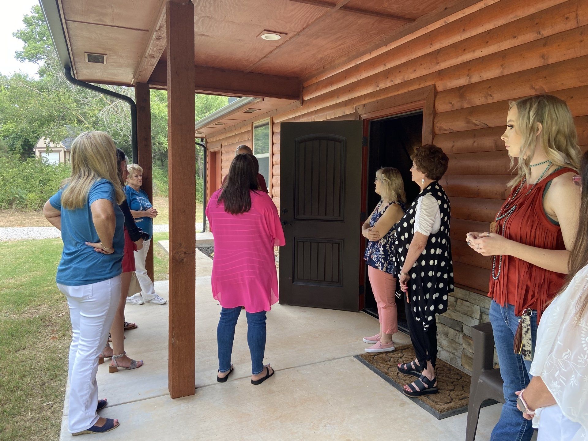 A group of women are standing outside of a log cabin.