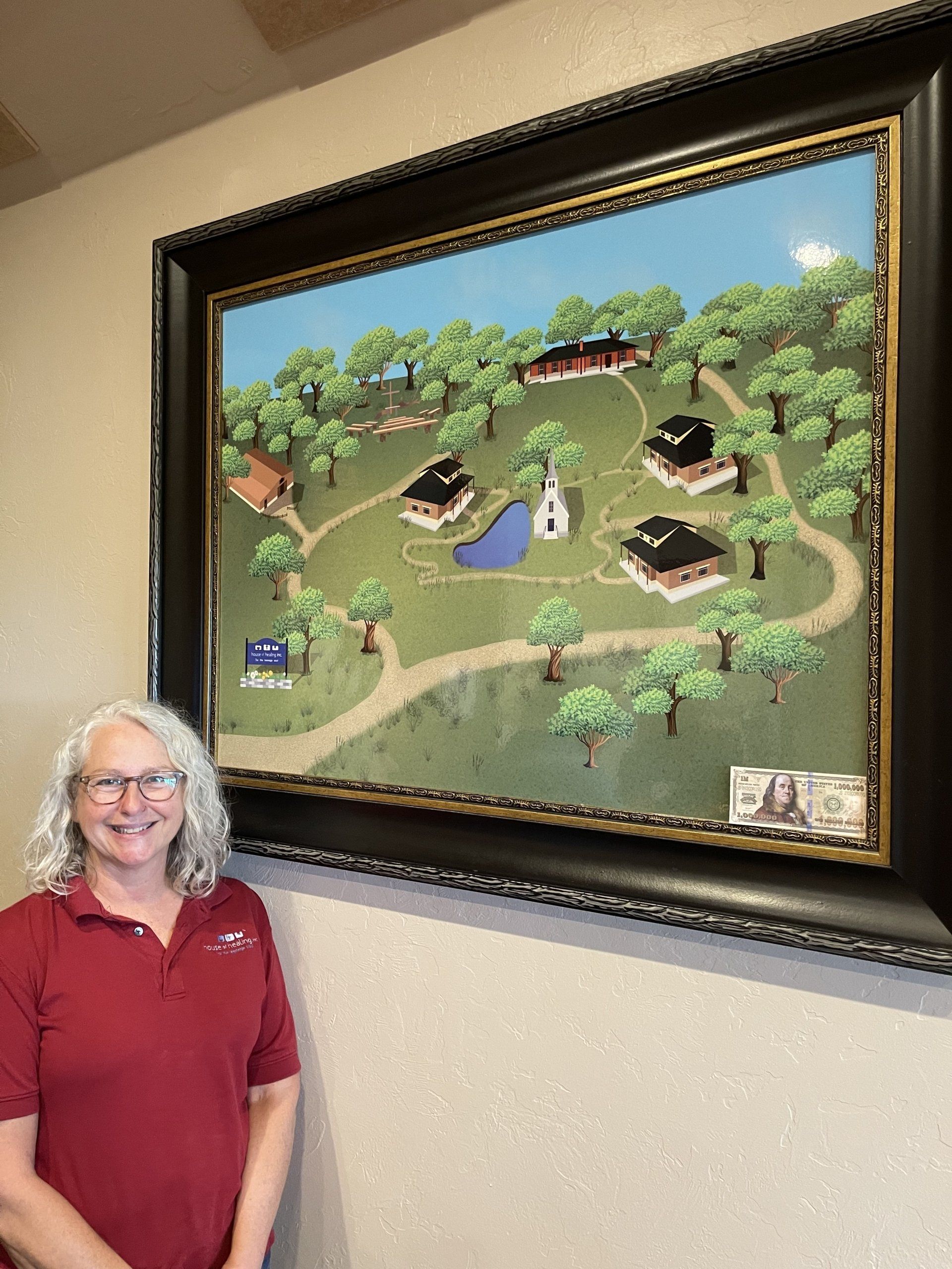 A woman in a red shirt is standing in front of a large painting on a wall.