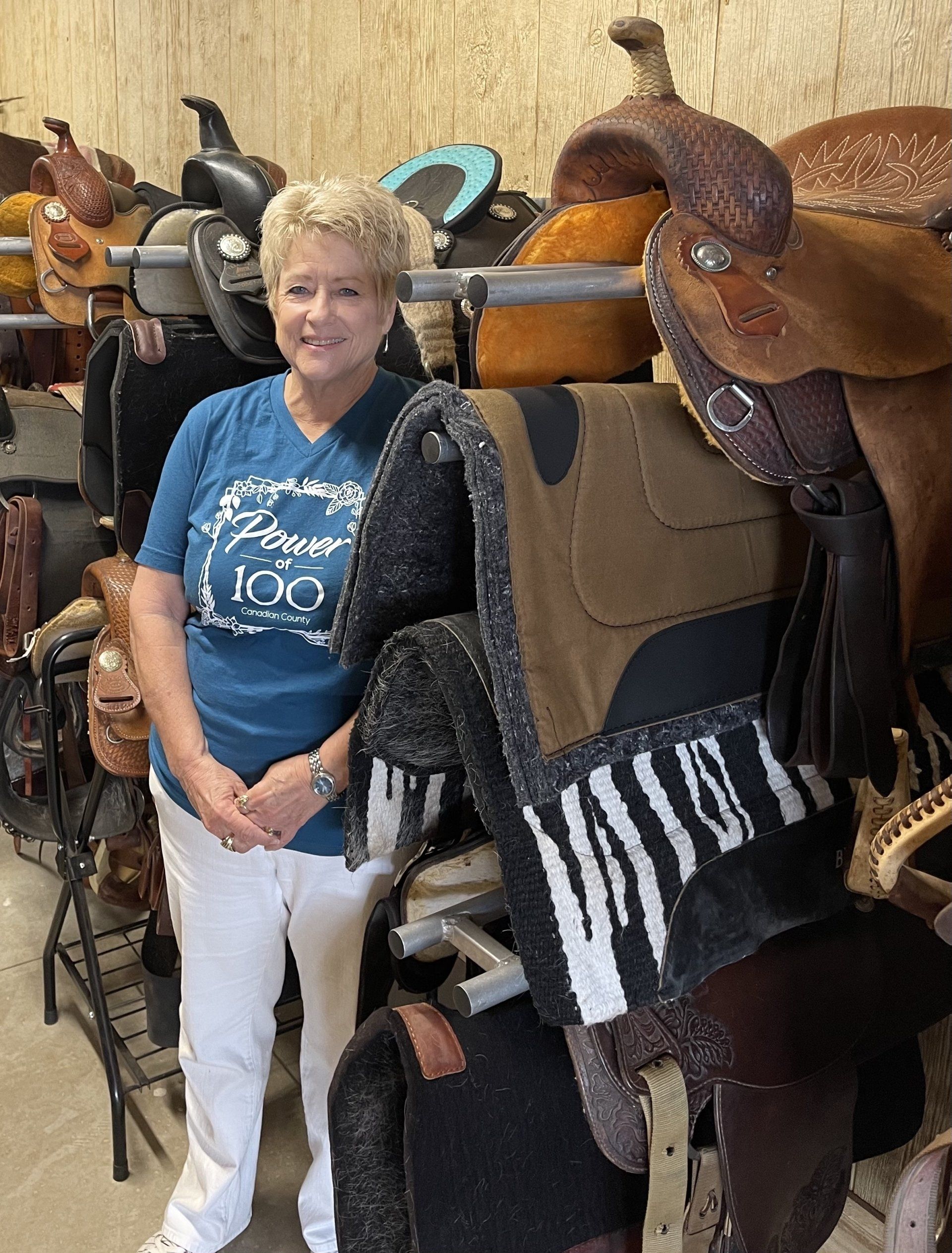 A woman is standing in front of a row of saddles.