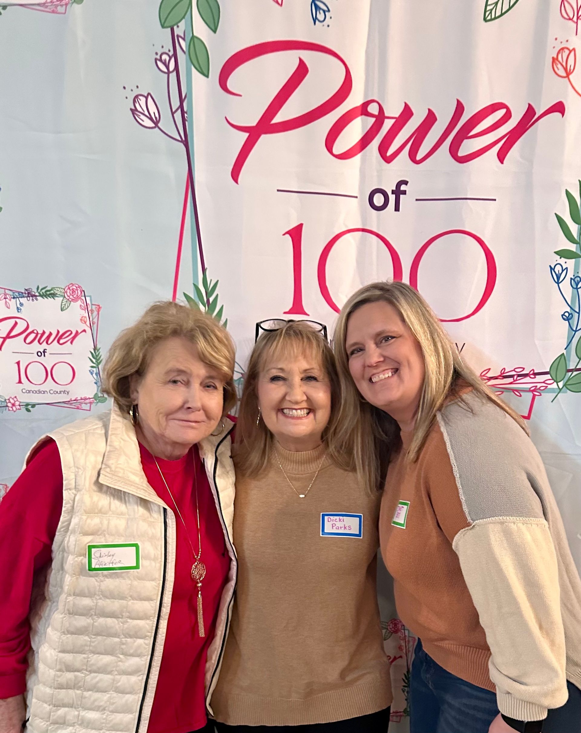 Three women are posing for a picture in front of a power of 100 sign.