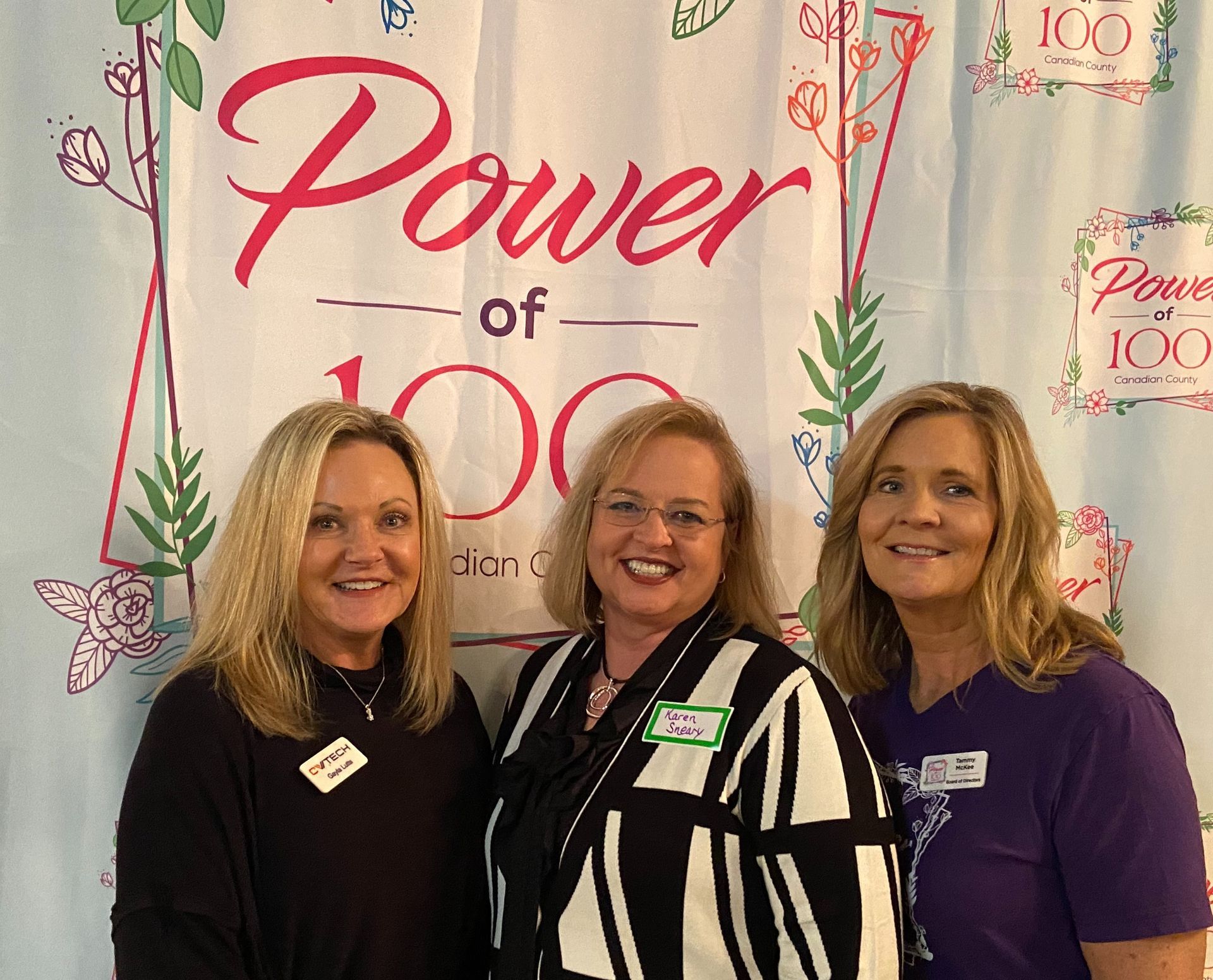 Three women are posing for a picture in front of a power of 100 sign.