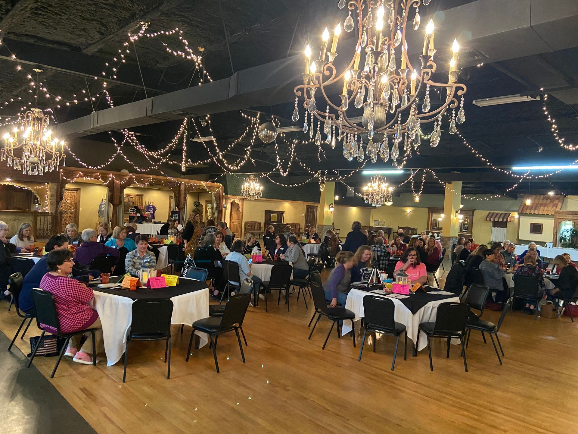 A large room with tables and chairs and a chandelier.