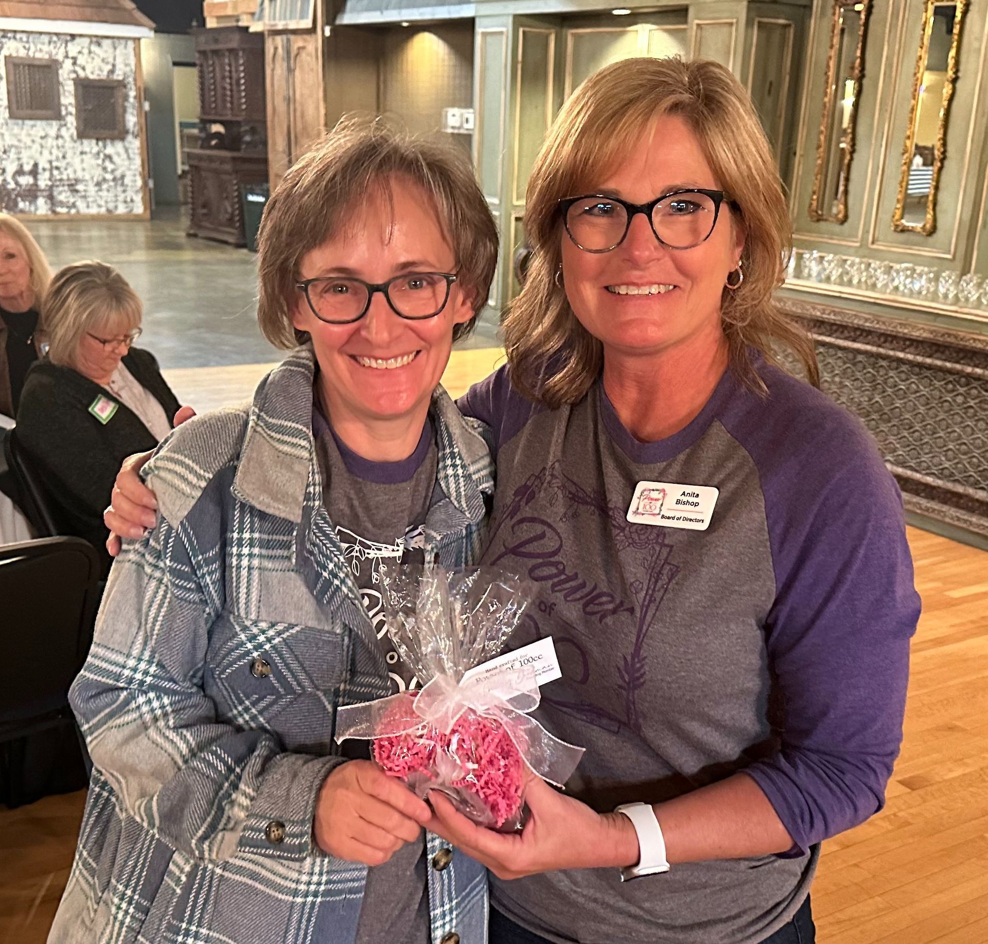 Two women are posing for a picture and one of them is holding a bag of candy.
