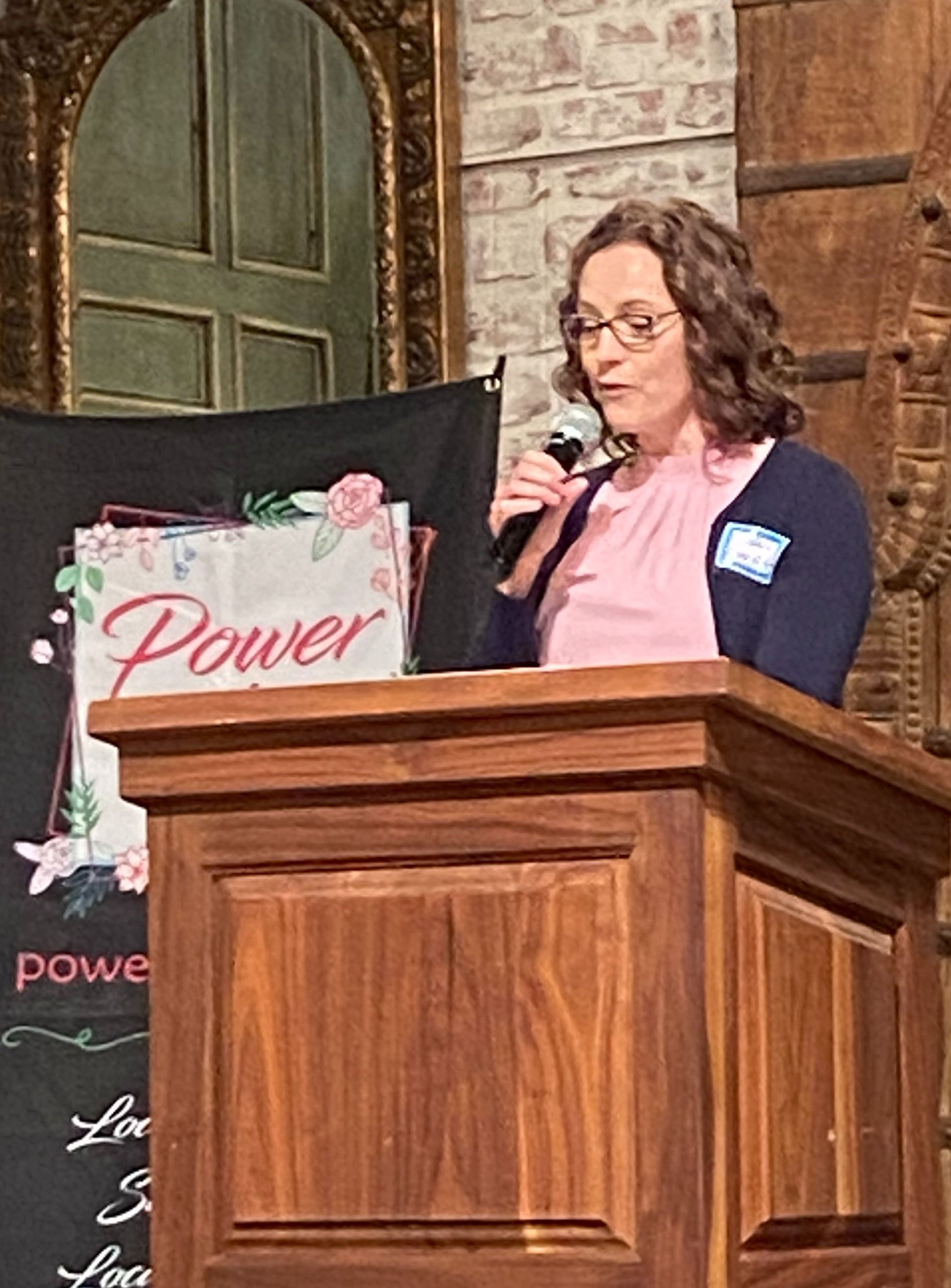 A woman is standing at a podium speaking into a microphone.