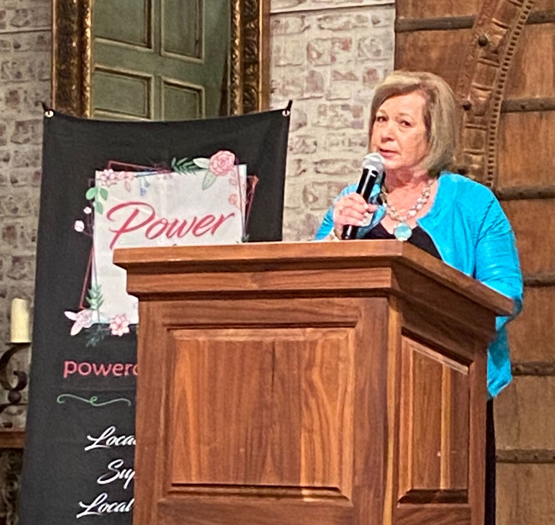 A woman is standing at a podium holding a microphone in front of a sign that says power