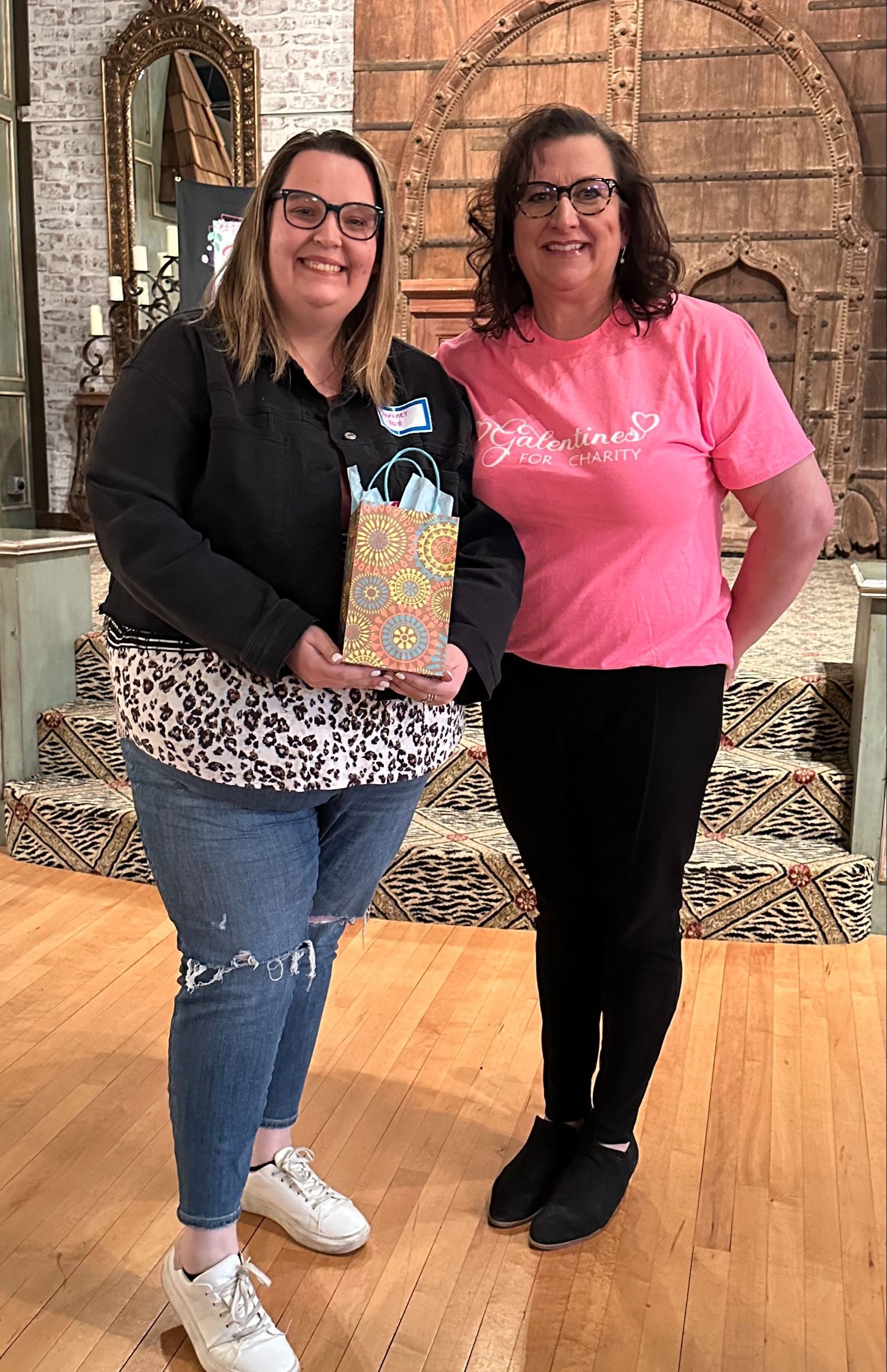 Two women are standing next to each other on a wooden floor.