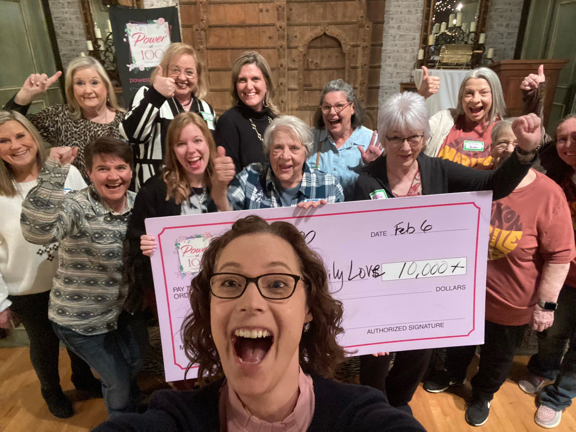 A group of women are holding a large check and giving thumbs up.