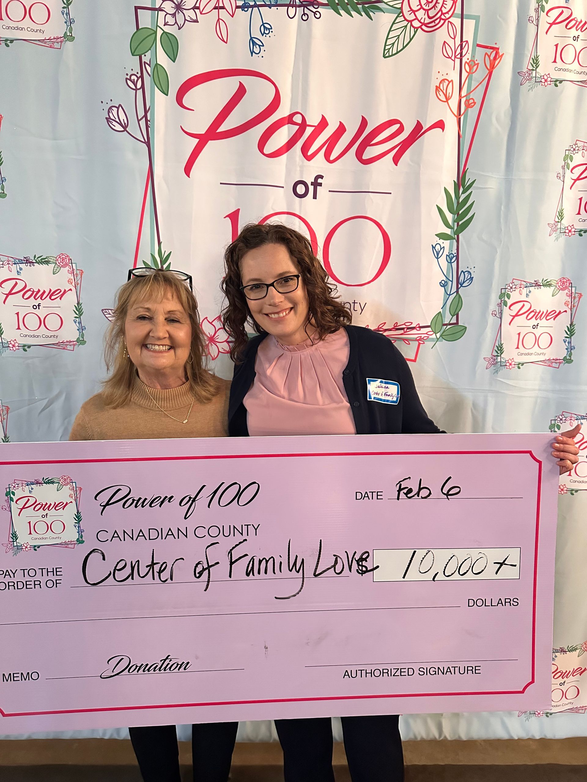 Two women are standing next to each other holding a large pink check.
