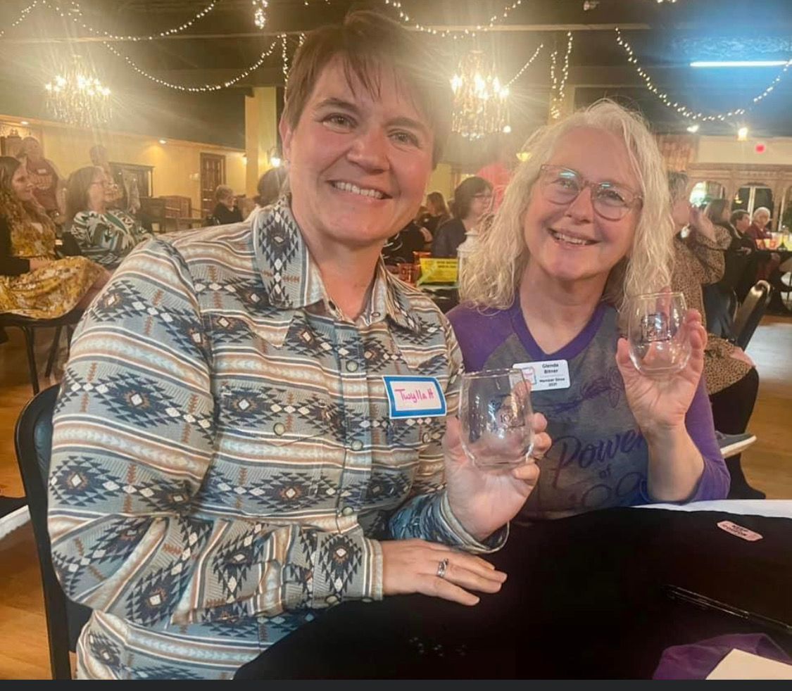Two women are sitting at a table holding wine glasses and smiling.
