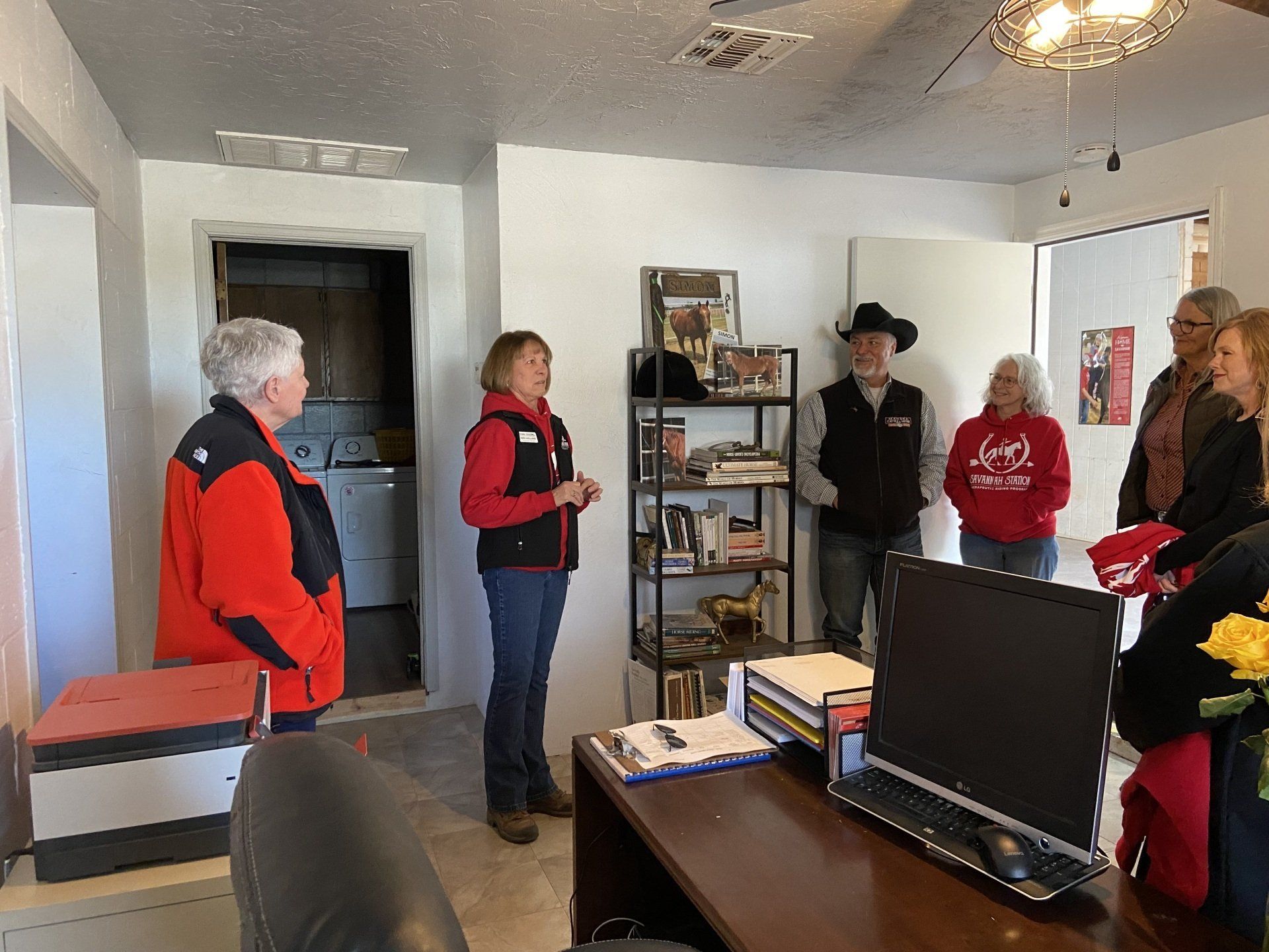 A group of people are standing around a desk in a room.